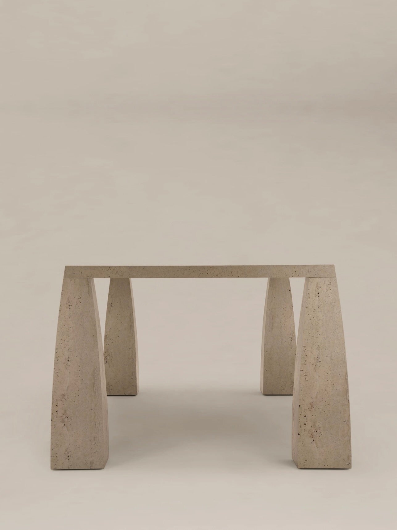 The "Khram" Dining Table by AÈDE Studios is a minimalist piece featuring a rectangular stone top with a trapezoidal shape, supported by four wide, tapering legs. Set against a light, neutral background, it offers a smooth and natural texture that evokes communal dining in medieval Russian architecture while maintaining a simple and modern design.