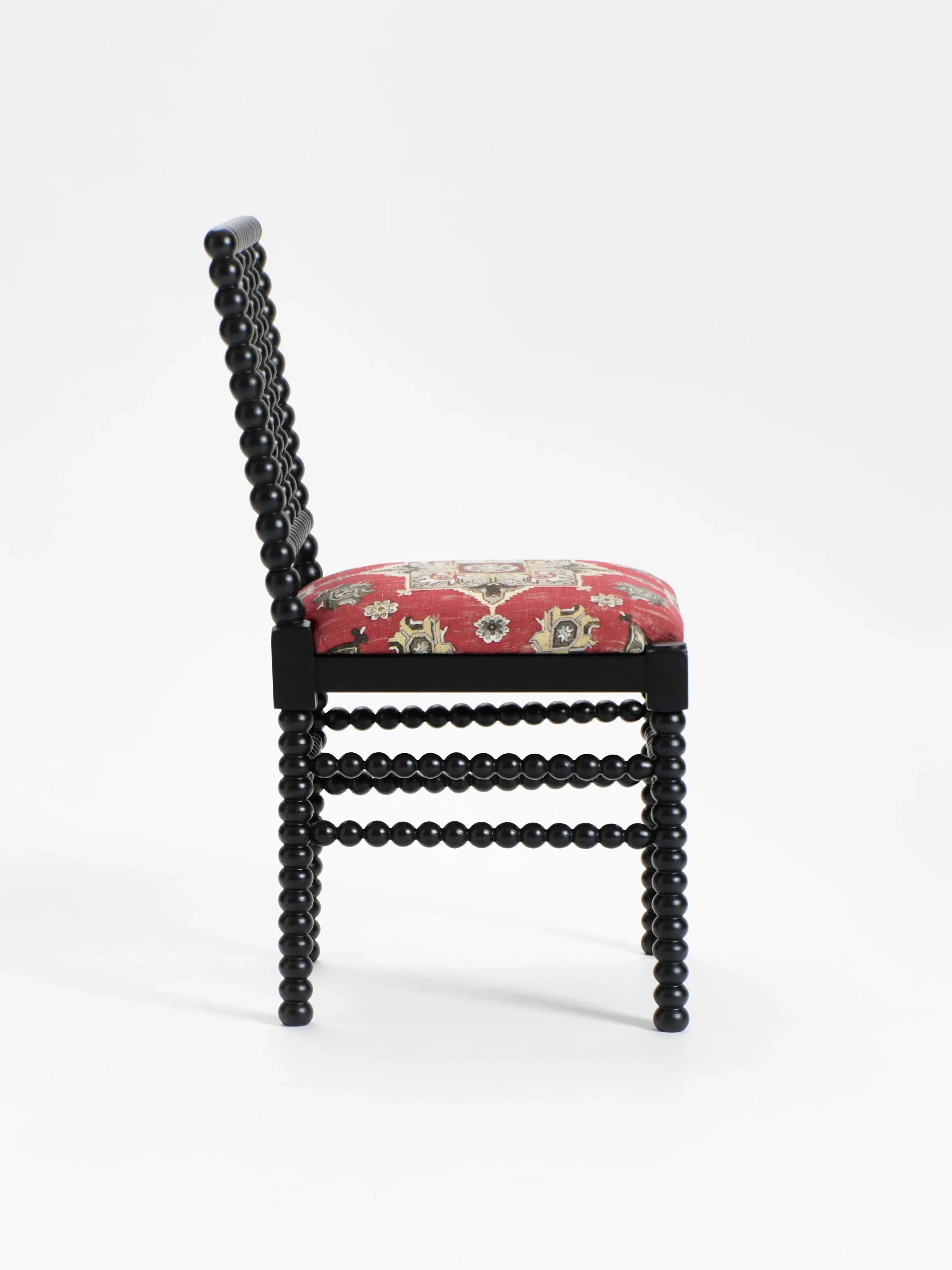 A side view of the "Bolha" Chair by Project 213A highlights its elegant wood-turned detailing on the legs and backrest, enhancing the dark wooden frame. The upholstered seat features a red fabric with an ornate floral design against a plain white background.