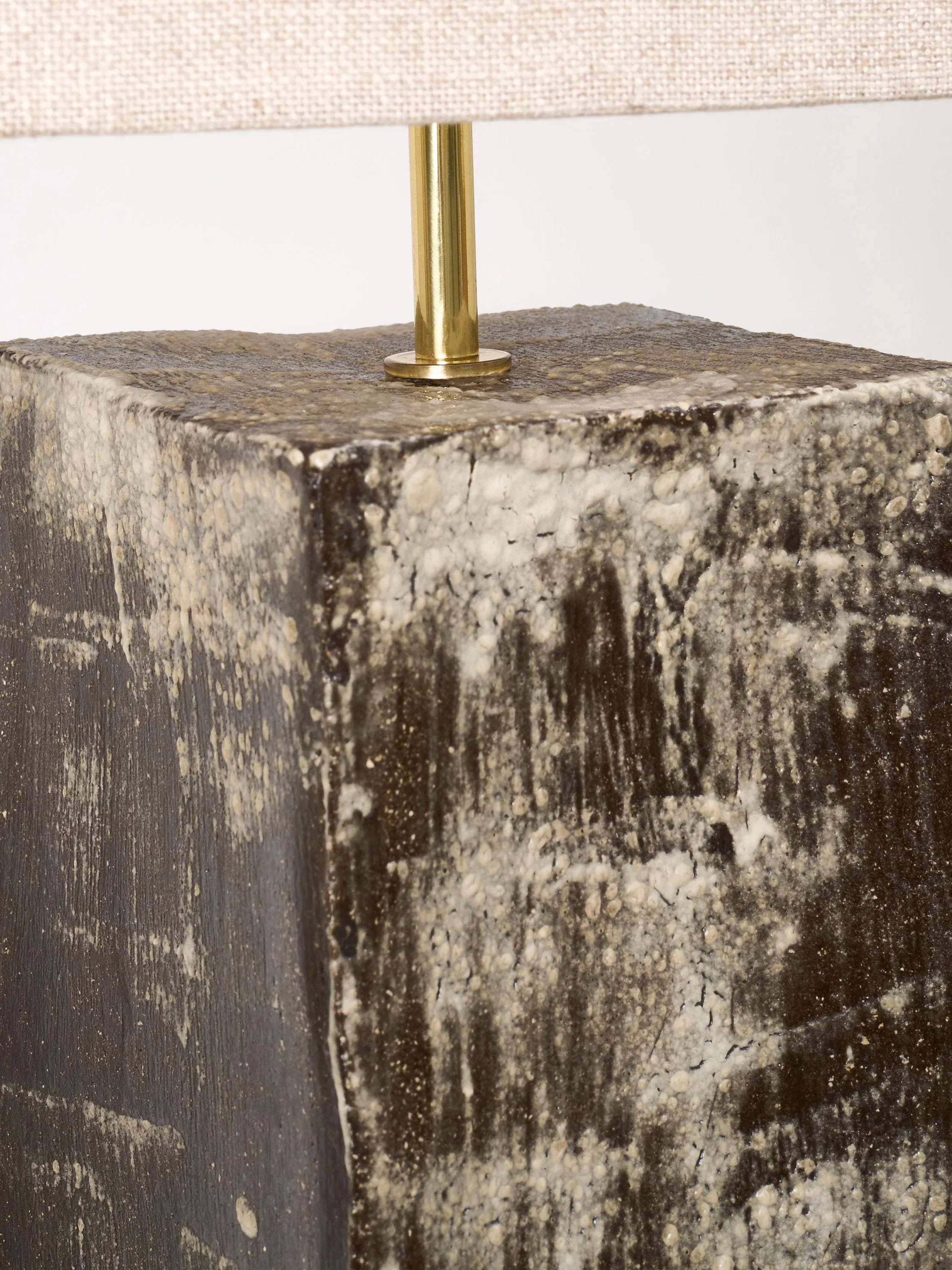 Close-up of Project 213A's Rectangular Ceramic Table Lamp, showcasing a handmade base with stone-like earthy patterns in gray and brown, paired with a brass stem. The base has a natural, rugged feel, and a fabric shade is partially visible at the top.