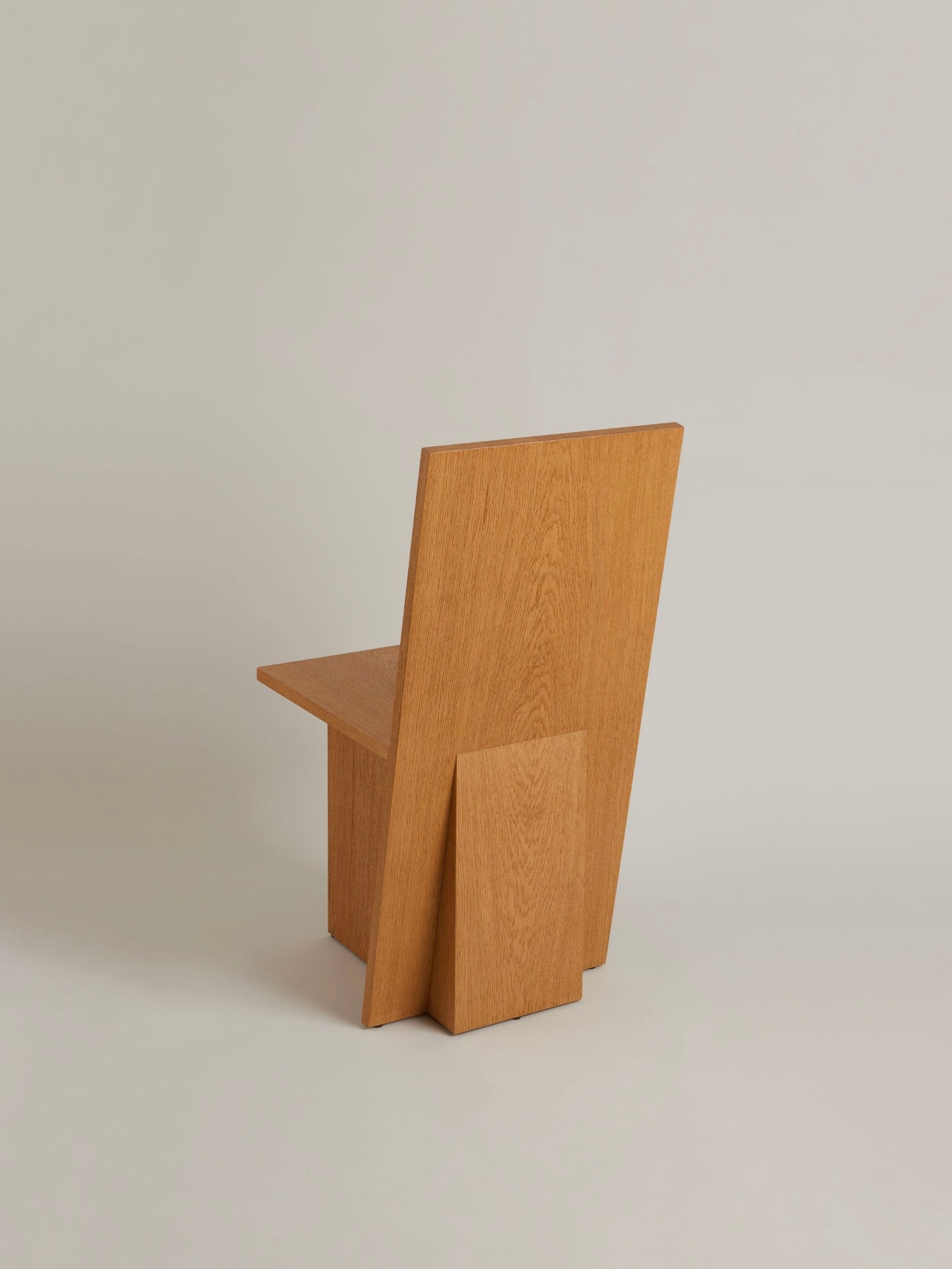 La Coupe: A minimalist modular chair by HAUVETTE & MADANI, crafted from brushed oak and showcasing a geometric design with flat surfaces and sharp angles, all set against a light grey background.