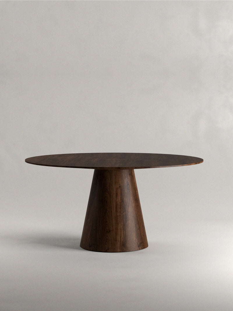 The Siete Studio 'Totem' Dining Table is handcrafted from solid walnut, showcasing a smooth, dark finish and a single wide conical base, elegantly set against a plain gray background.