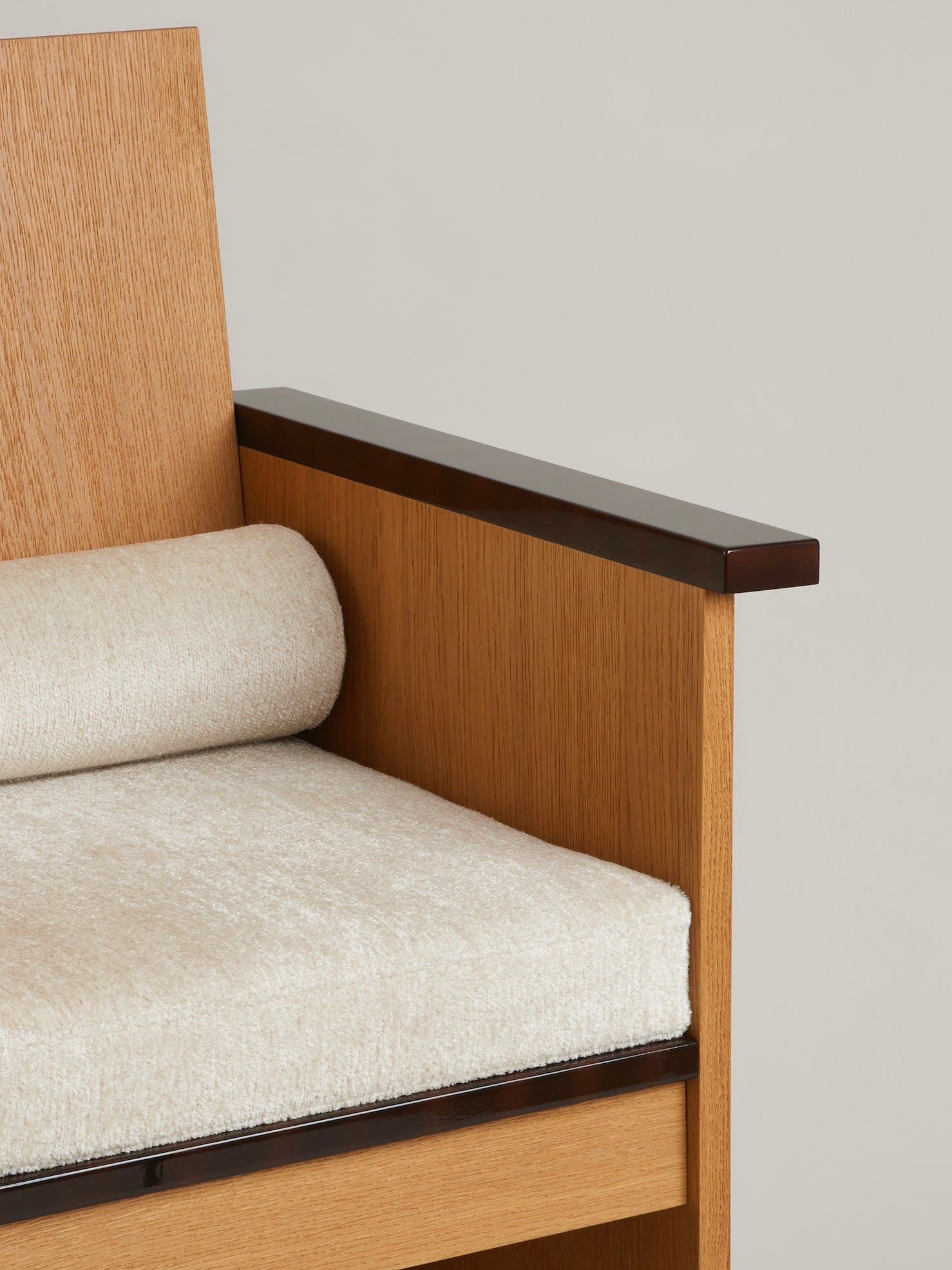 Close-up of the "Le Parfait" Armchair by HAUVETTE & MADANI, showcasing its modern wooden design with a light beige cushion and lacquered armrests. The vertical backrest, crafted from brushed oak, provides a striking contrast to the smooth and minimalistic style of the seating area and cushion.