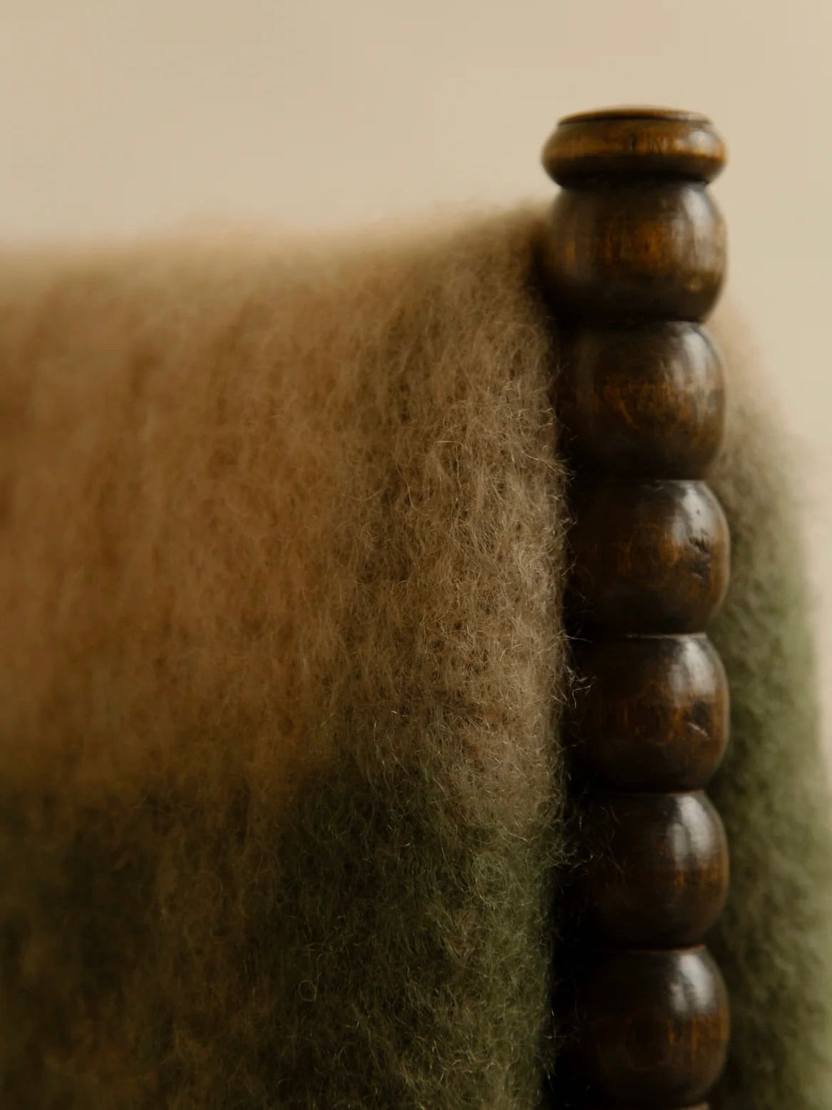 The "Arbor no. 2" throw by The Wren features a luxurious, textured moss-green wool fabric that beautifully complements its dark wooden design with rounded, bead-like accents, resulting in an eco-friendly masterpiece.