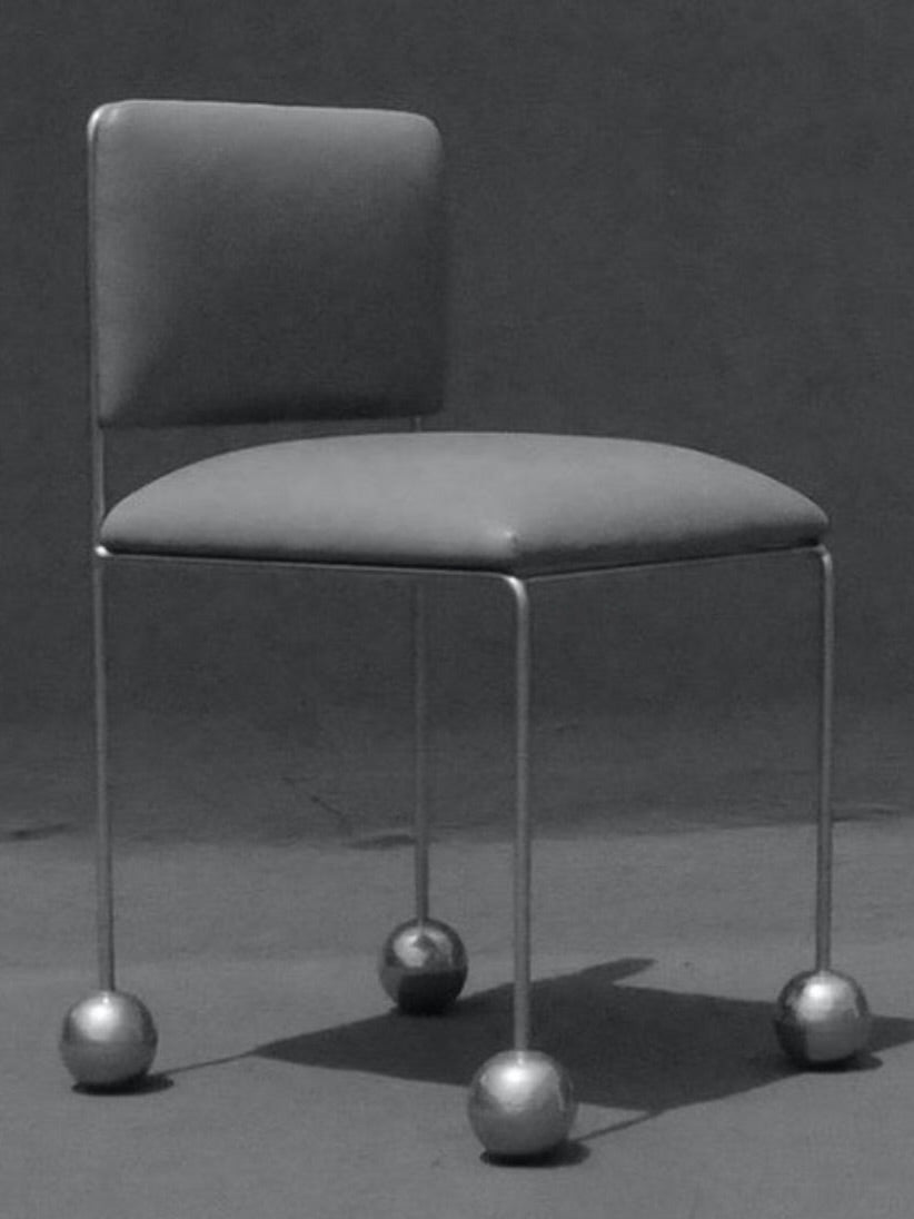 Introducing the 'Ball Foot' Chair by Panorammma: a minimalist masterpiece with a rectangular backrest and vegan textile upholstered seat. It features thin metal legs ending in spherical feet, all beautifully contrasted against a dark background.