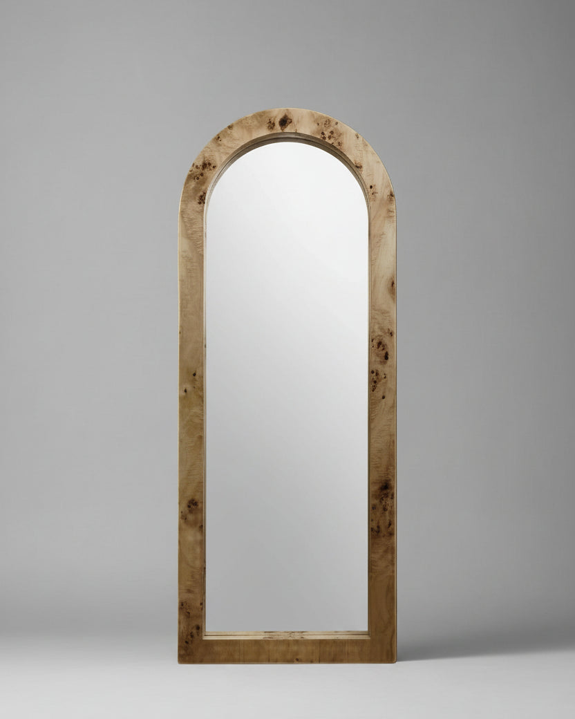 A Ransom & Dunn Arc Burl Wood Floor Mirror, featuring a natural ash burl wood frame, stands upright against a neutral beige background, exuding a subtle nod to neoclassical architecture.