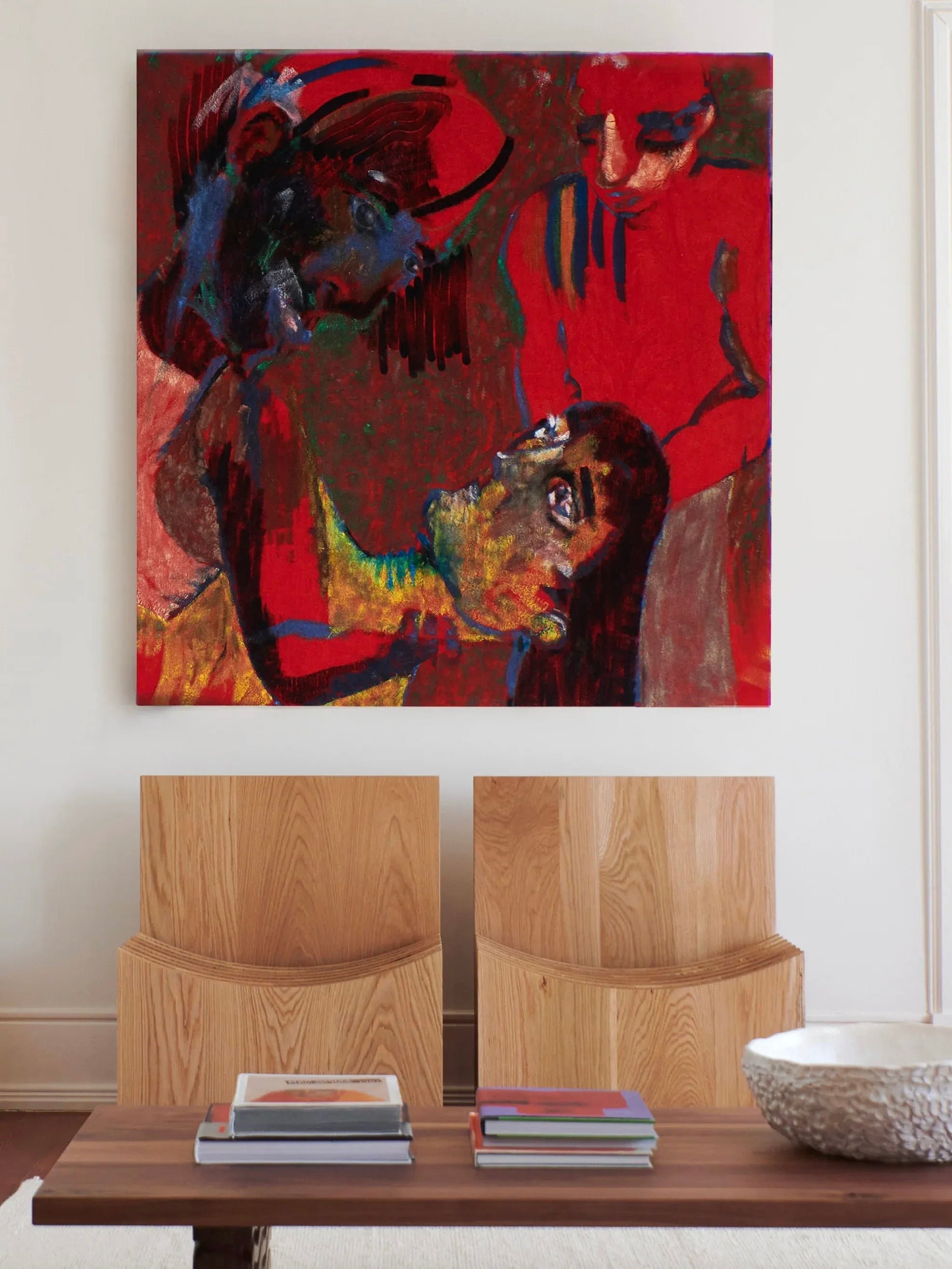 A modern living room features a large abstract painting with bold red, blue, and yellow tones, depicting distorted human figures. Below the painting are two minimalist Melides Chairs from Project 213A, hand-crafted from solid oak, and a low wooden table adorned with several books and a decorative bowl.