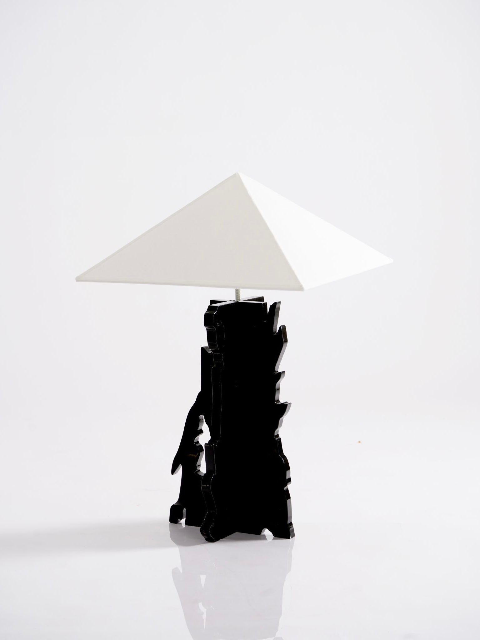 The Bird" Table Lamp by Ochoa Rocabert is a modern piece featuring a geometric white pyramidal shade and a unique jagged black base, seamlessly integrating abstract forms into its design.