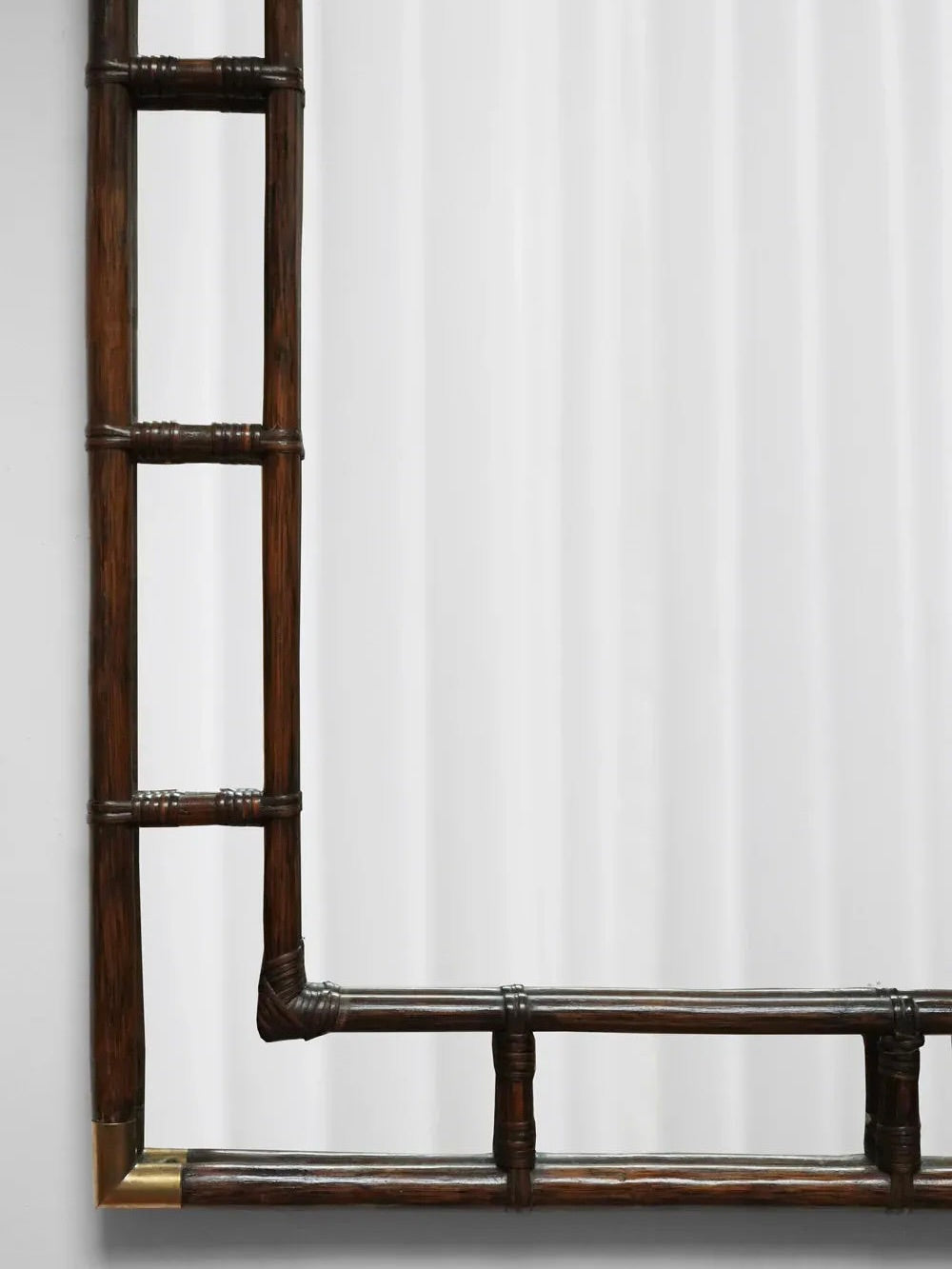 The Brown Rattan and Brass Mirror from Barracuda Interiors, crafted in the 1970s, showcases a bamboo-inspired design with rattan accents. Its vertical and horizontal elements form an L-shape against a white background, while the dark brown hue provides a striking contrast to the light backdrop.