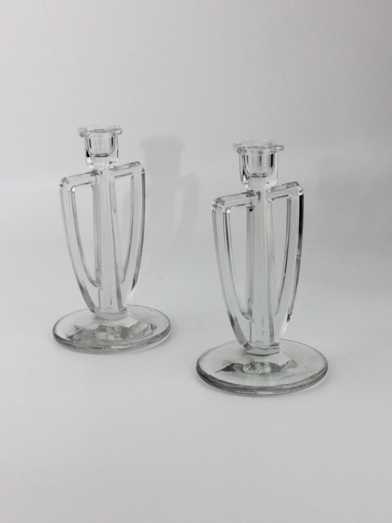 Two Crystal Candle Holders from Boga Avante Shop, featuring an Art Deco design with geometric lines and a round base, stand on a plain white background. Their sleek, symmetrical appearance evokes the elegance of clear crystal chandeliers and the minimalist, timeless allure of classic decor.