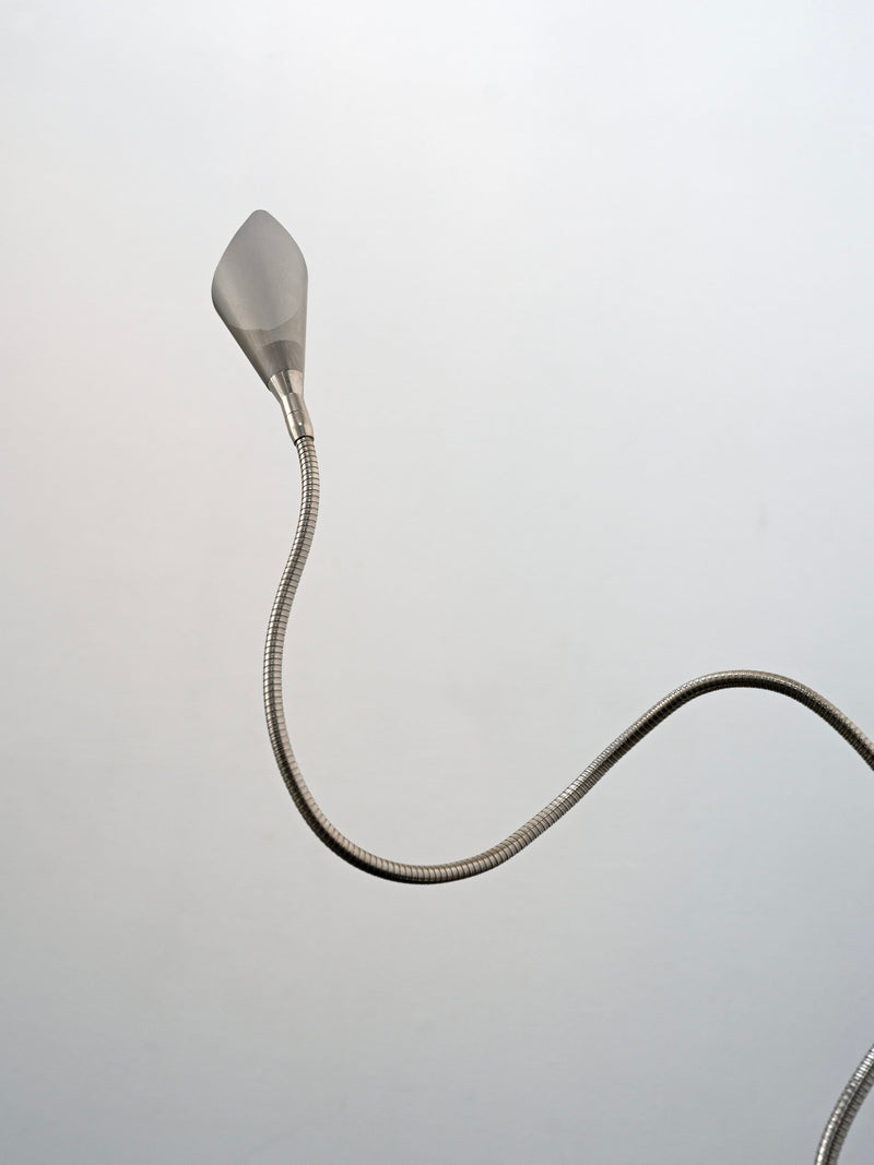 The Italian Chrome Table Lamp by Tom Bogle, c.1990 features a flexible metal hose and brushed metal nozzle, curving in an S-shape against a plain light gray background, evoking classic Italian design.