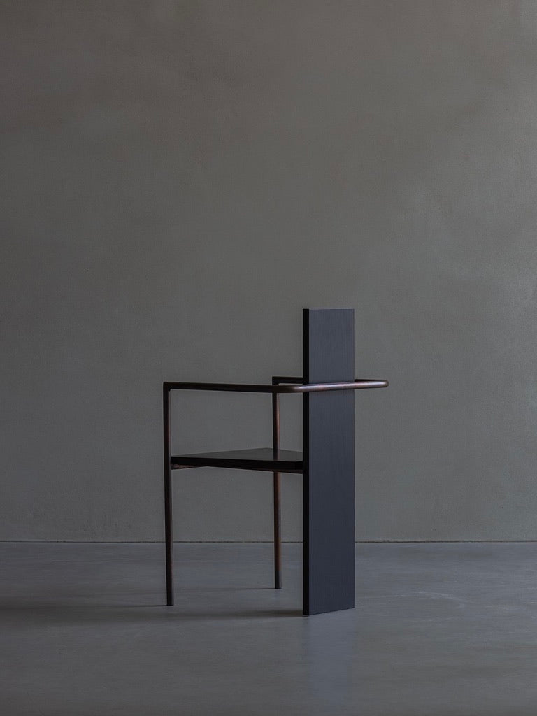 The Jonas Bohlin - CONCRETE - black chair by Bicci de' Medici features a minimalist design with a sleek black finish, thin metal frame, and tall flat backrest. Set against a plain gray background, it embodies a modern and artistic Concrete Chair aesthetic.