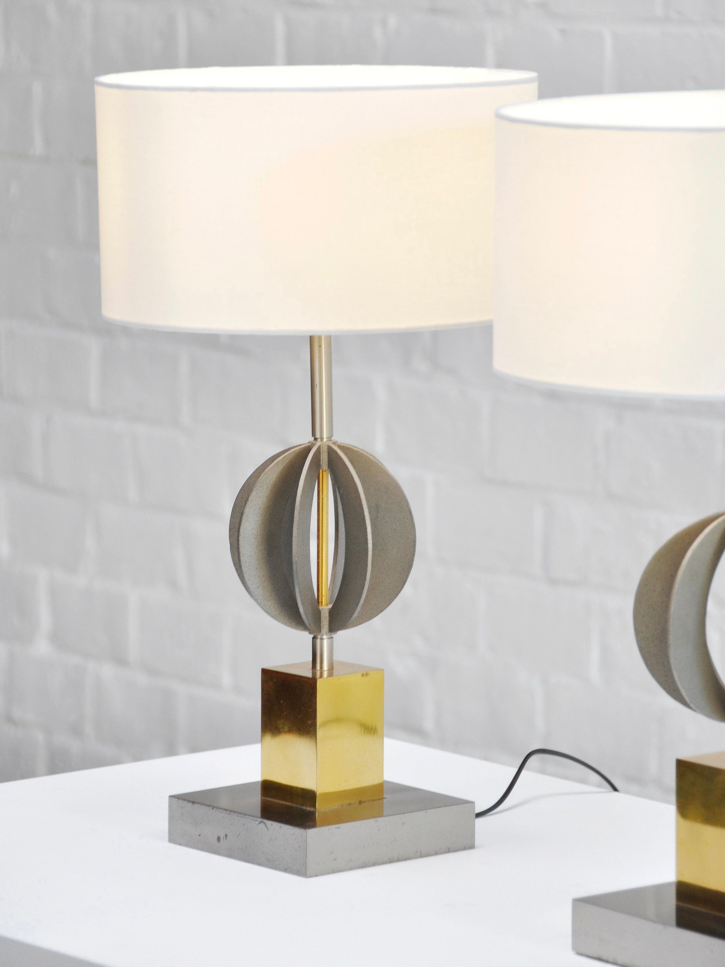 The Introverso Pair of Italian Geometric Table Lamps from the '70s boasts a modern sculptural design with a white cylindrical shade and a geometric metal base of spheres and a gold cube, elegantly displayed on a white surface against a light gray brick wall.