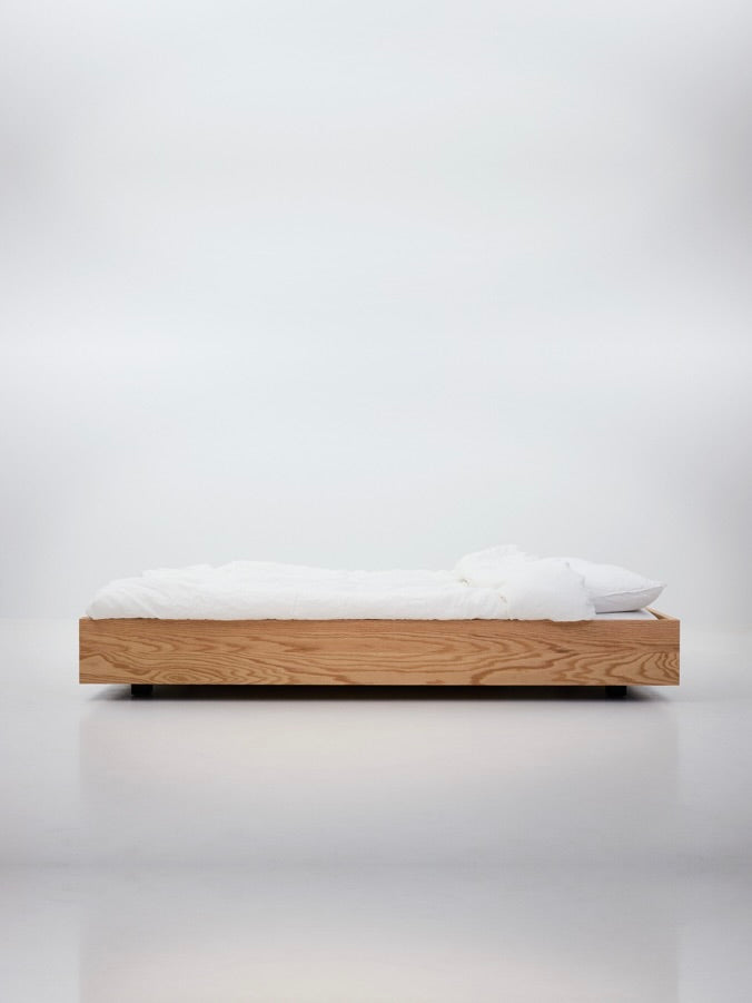 The Floating Bed - Natural by Axel Wannberg is a minimalist red oak floating bed with white bedding and a pillow, showcased against a plain white background.