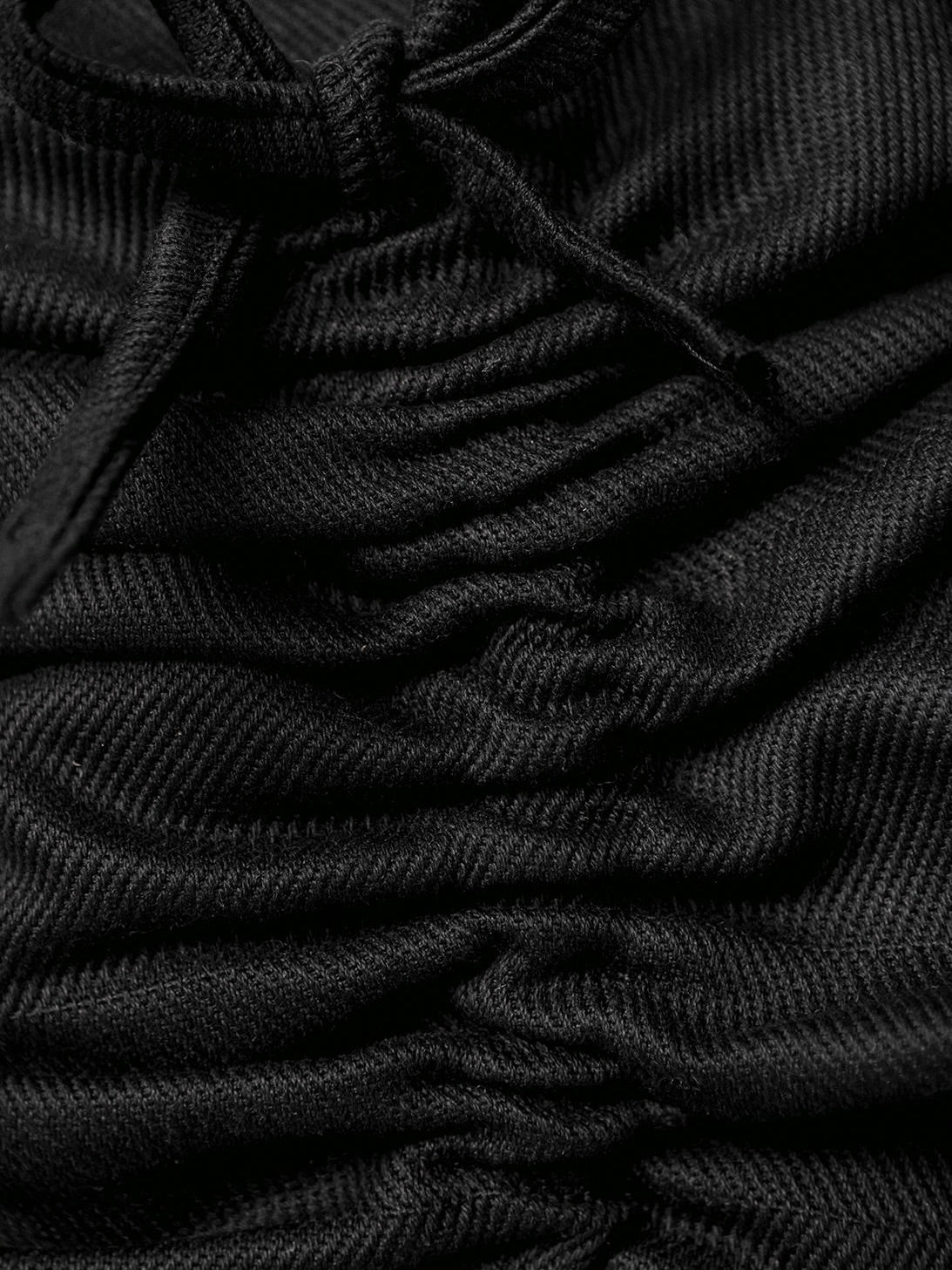 Close-up of the Daphne Charcoal Cushion by SANTA LIVING reveals black fabric with a gathered, ruched texture and tied strings. Its soft, ribbed pattern creates dynamic shadows and highlights—a testament to exquisite home textiles handmade in Barcelona.