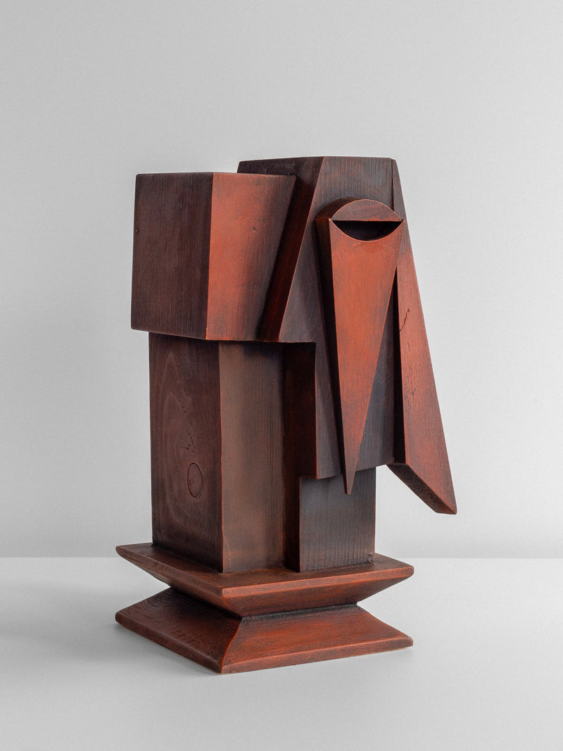 The Vintage Cubist Sculpture by Atelier Boulogne from Spigel is a minimalist figural wood sculpture featuring geometric shapes and angular designs. Crafted from dark brown and reddish wood, it creates an abstract form that evokes cubism, mounted on a simple rectangular base. The plain white background perfectly accentuates this masterpiece.