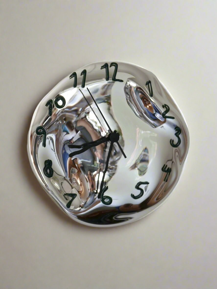 Experience the art of time with Silverclock - Green and Black by Silje Lindrup, a handcrafted Danish wall clock featuring a surreal, melted design inspired by Salvador Dalí. The warped clock face and numerals give an unevenly spaced appearance, and the irregularly bent hands add to its unique charm. Its reliable quartz mechanism stands out against the plain white background, ensuring accurate timekeeping.