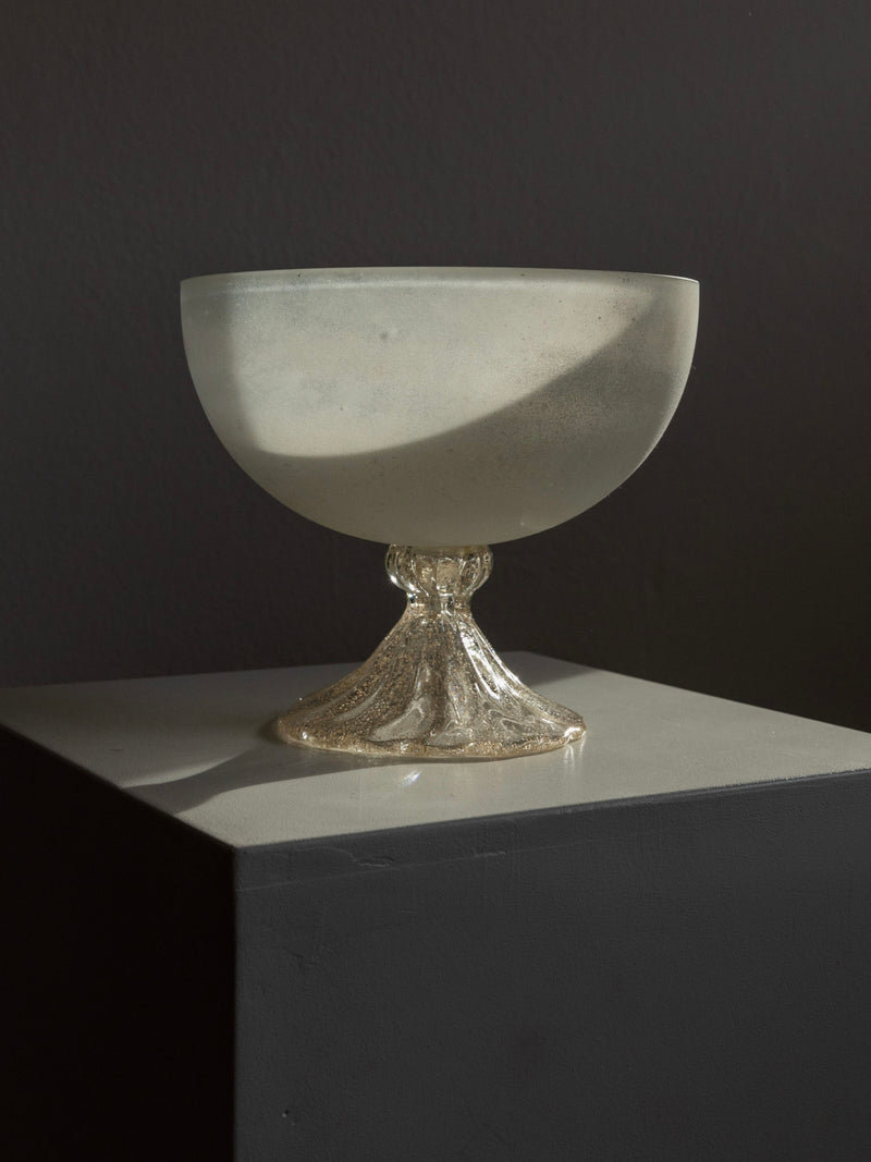 A vintage Bottega Jacobs Murano Glass Bowl from Italy's 1970s features a textured base on a dark pedestal, with lighting casting soft shadows to accentuate its translucent, matte finish.