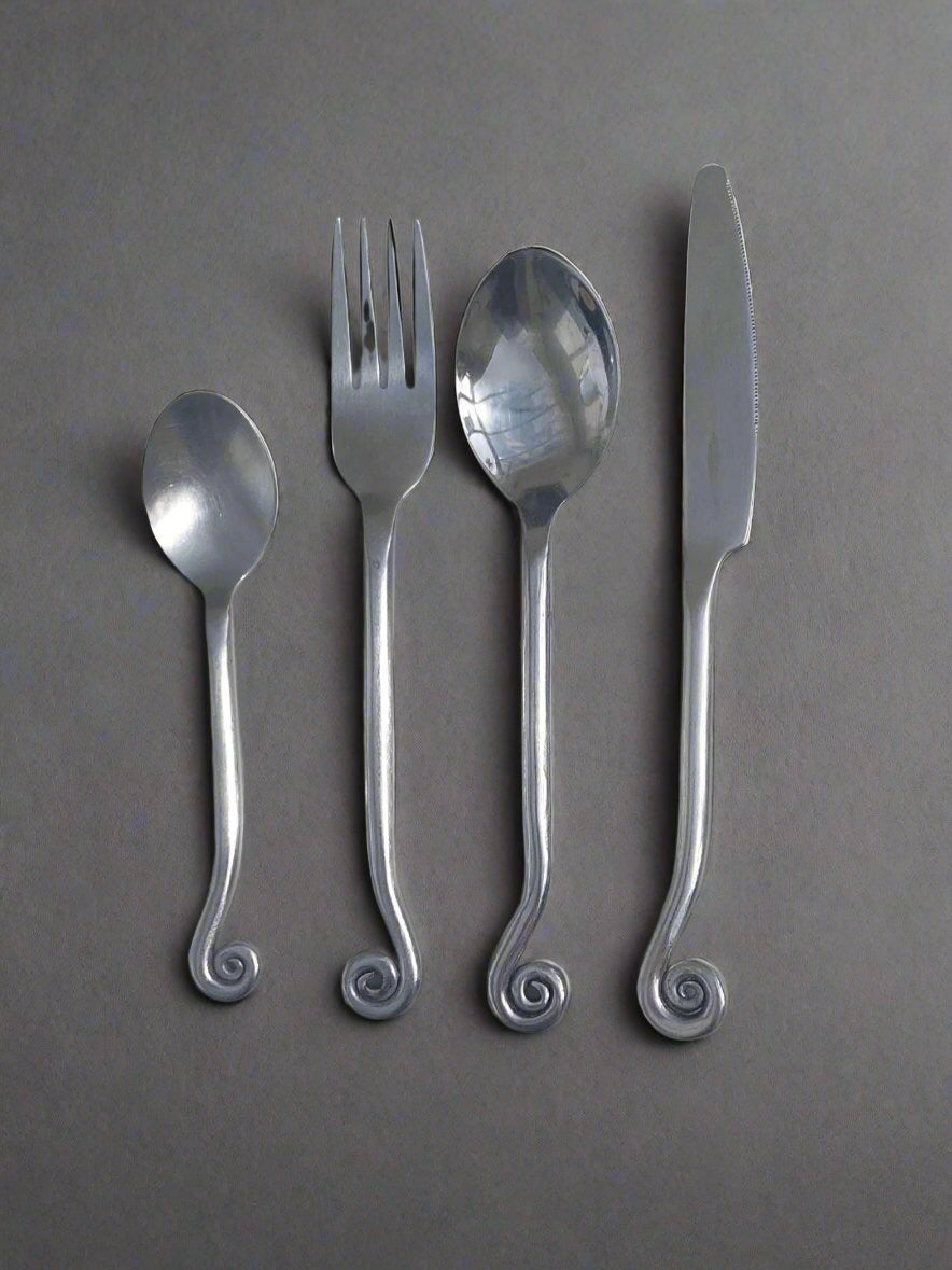 Introducing the Set of 4 Swirling Cutlery by Les Objoies, featuring a fork, knife, spoon, and soup spoon. Crafted from stainless steel with a sophisticated gray backdrop, each piece boasts a distinctive spiral design at the end of the handle.