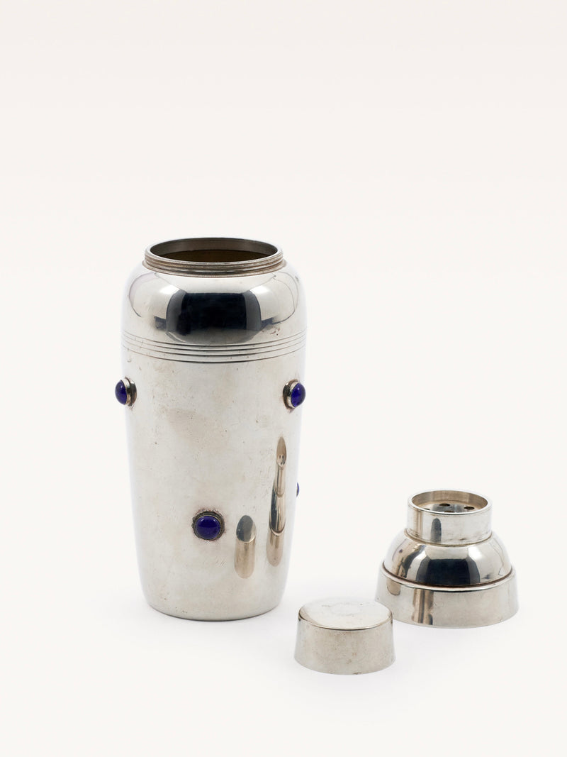 A sleek Shaker with Blue Stones by Galerie MLS features a chrome cylindrical body with Cartier-style blue stone accents. The lid and cap are beside it, displaying the open shaker against a plain white background.