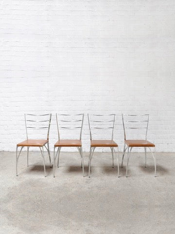 A set of four 'Organic' dining chairs by Erwan Boulloud from Introverso, featuring sculptural aluminum frames and brown seats, is aligned against a white brick wall. The concrete floor adds to the minimalist, industrial vibe characteristic of Boulloud's design style.