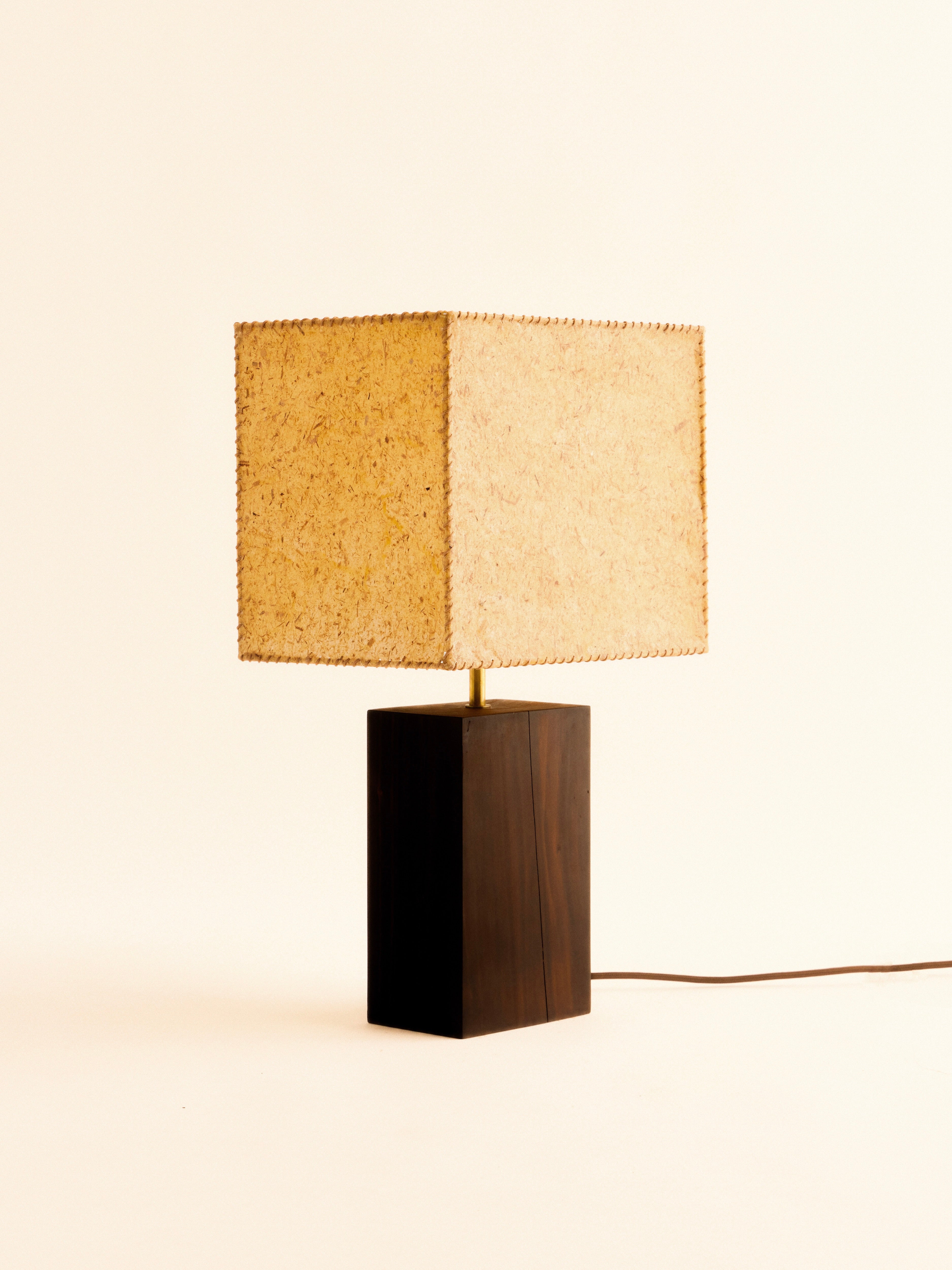 The 1948 Table Lamp by Lana Launay showcases a minimalist design with a rectangular banana fibre shade and a dark wooden base. Handcrafted in Sydney, this lamp is set against a simple, light backdrop, with the power cord discreetly visible on the right side.