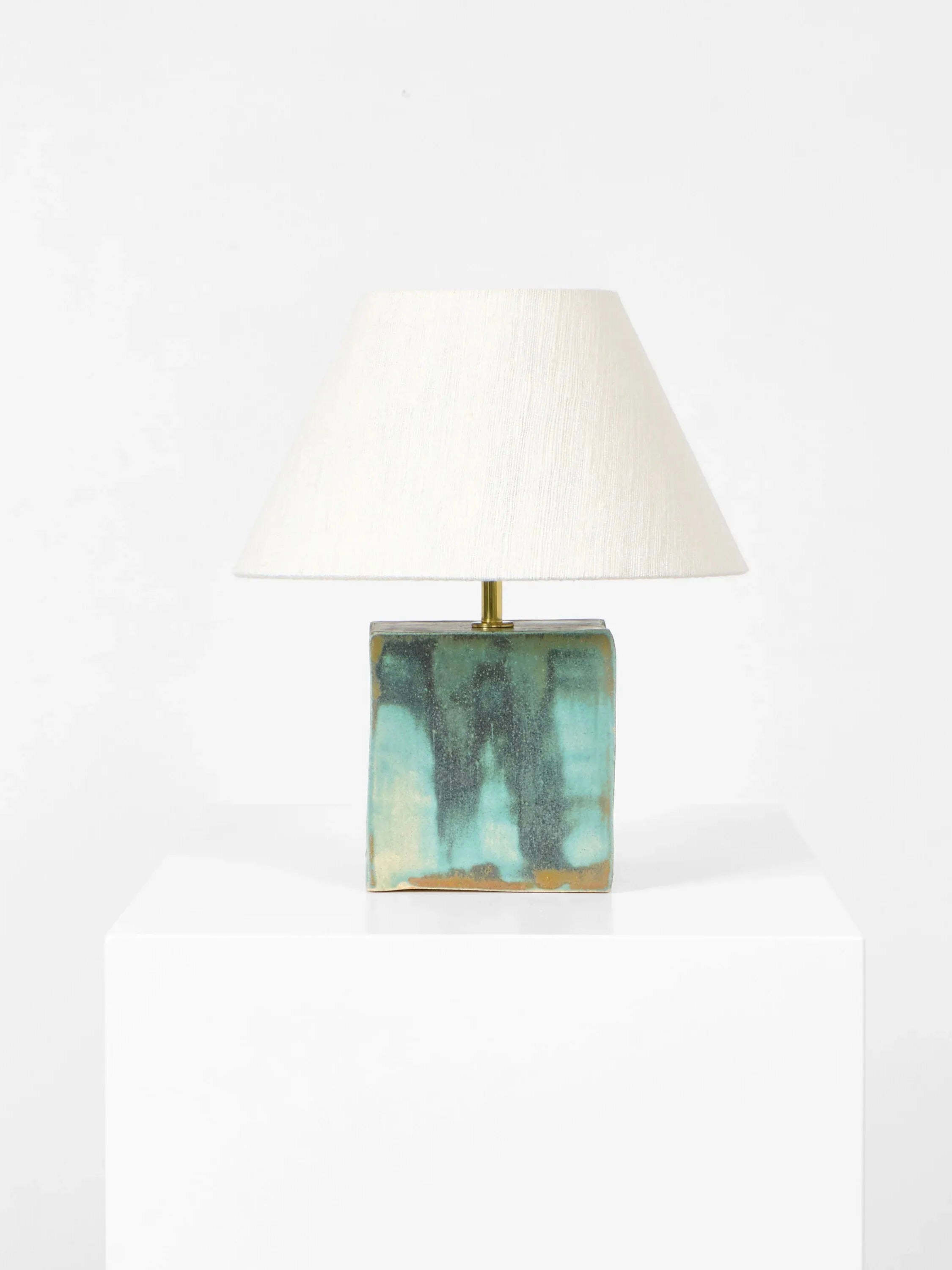 The Arouca Table Light by Project 213A features a cream conical shade on a white pedestal, with a square ceramic base in mottled green, blue, and brown. This handcrafted piece stands elegantly against a plain white background.