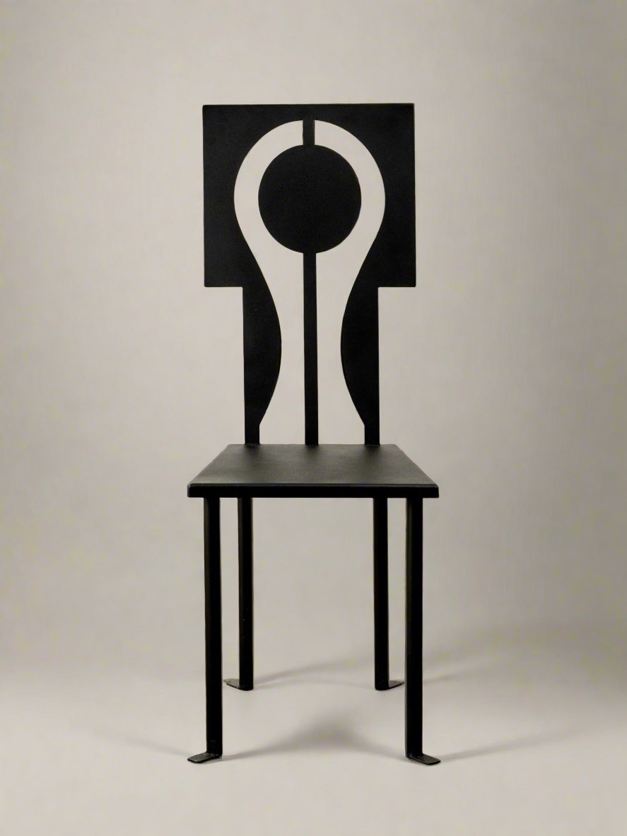 Meet the Luna Chair in Iron and Black Powder Coat by Animate Objects, a contemporary addition to the Rèveuse collection. It features a sleek black seat and legs with a high backrest adorned with an abstract design of circular cutouts and striking geometric shapes against white. This handcrafted masterpiece is perfectly suited for display on a wooden floor.