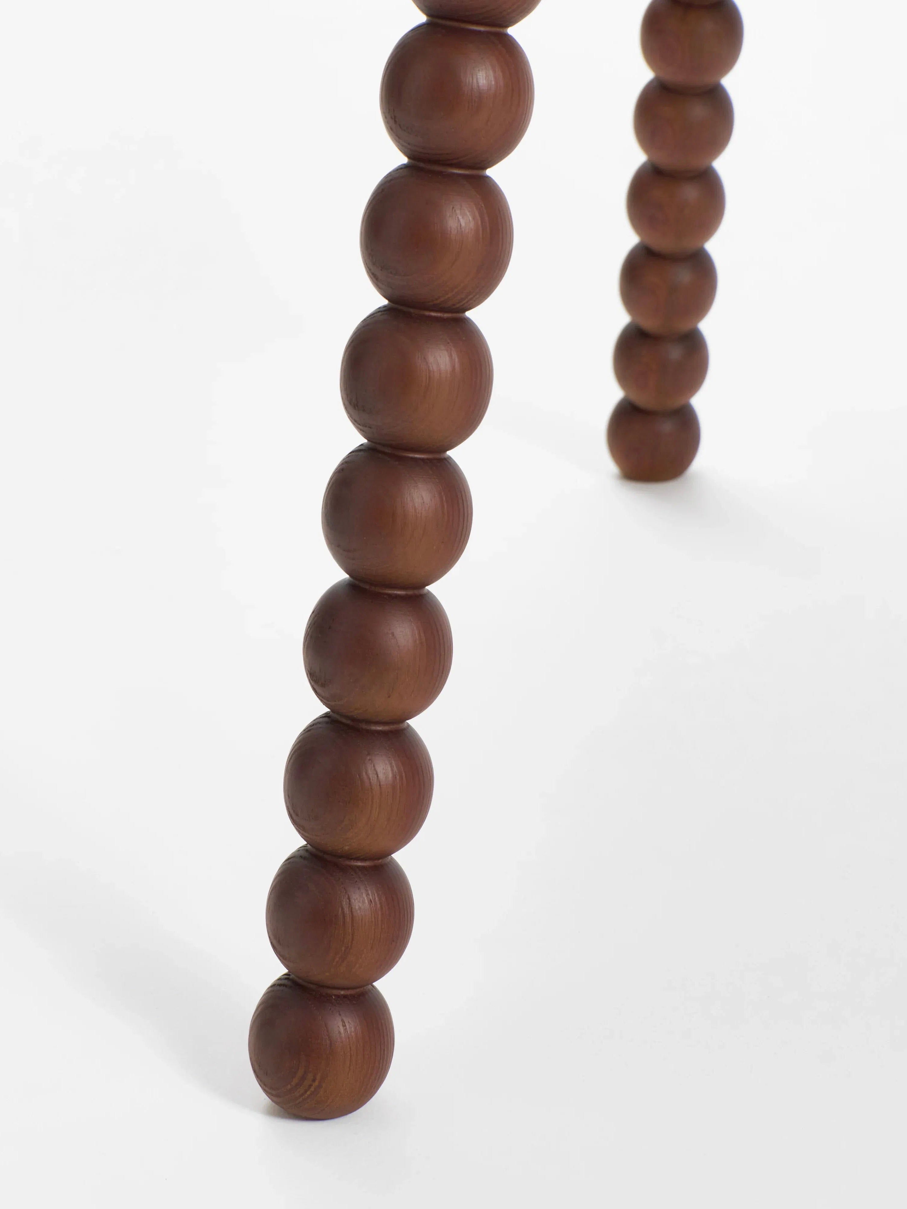 Close-up of a 'Bolha' dining table leg by Project 213A, showcasing intricate turned wood detailing with bead-like segments, set against a white backdrop. A similar leg is also visible in the background, part of the Bistro arrangement.