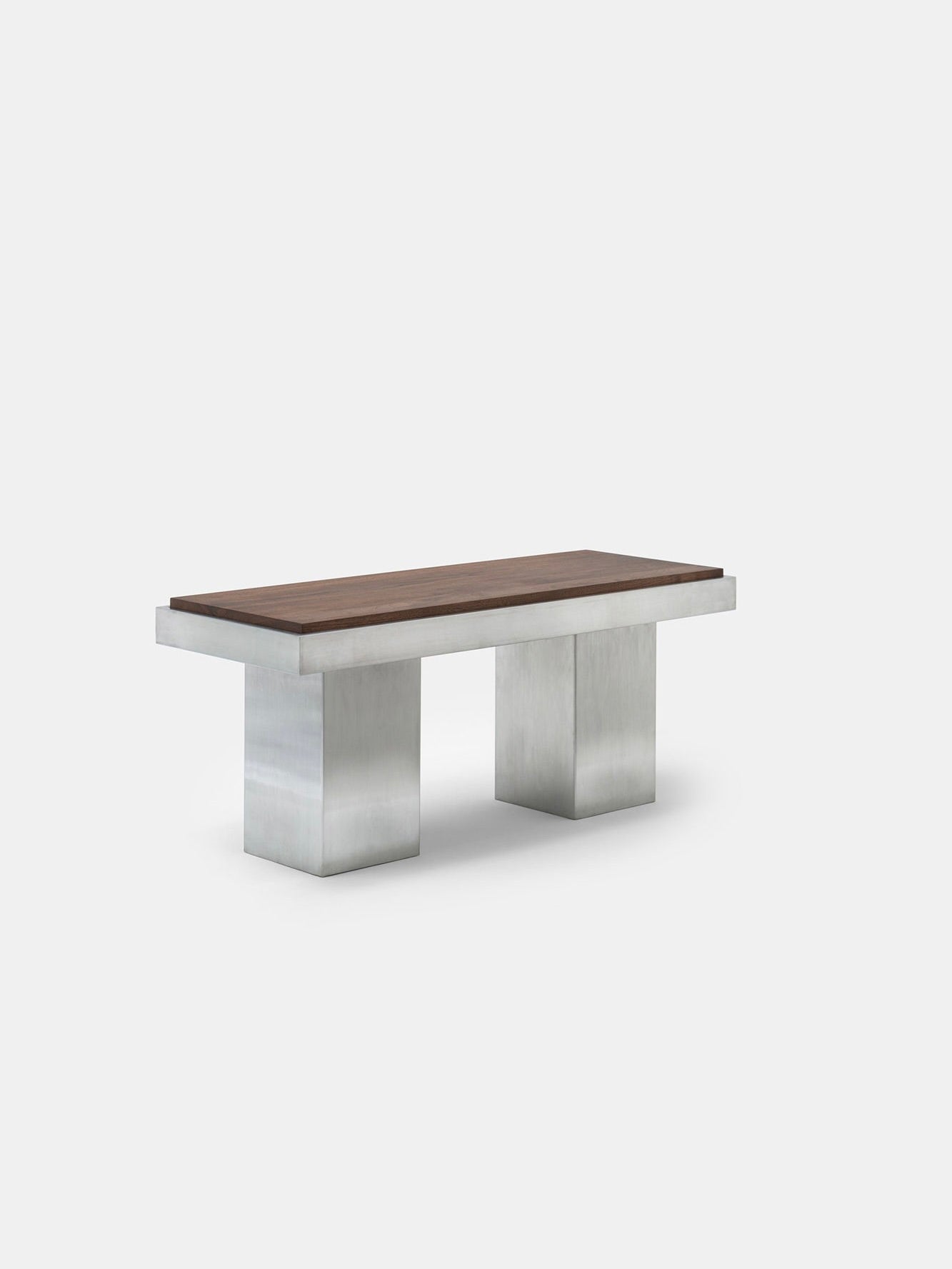 The Console Table 02 by Studio Vraco showcases a minimalist and sleek design with a dark wooden top and two rectangular brushed stainless steel legs, all against a simple light gray backdrop. Its modern aesthetic perfectly captures the essence of Bauhaus furniture by blending natural and industrial elements.