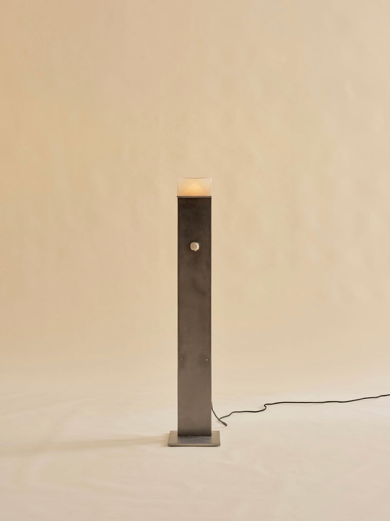 The Perceptions Floor Lamp by Known Work features a tall and slender dark metal design on a simple square base against a beige background, with a handcrafted spherical knob midway and connects to power via a black cord.