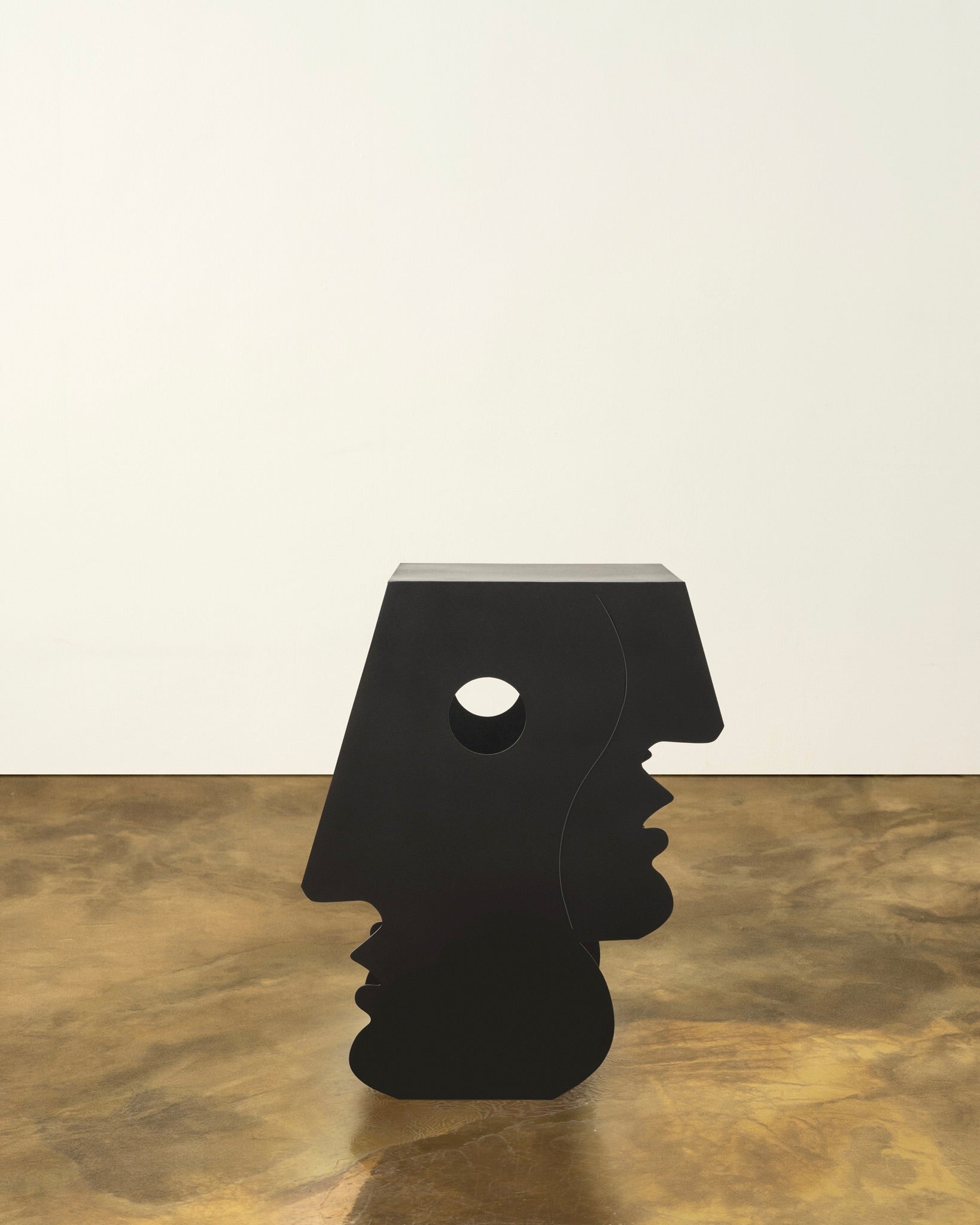 The "Lucia" Side Table in Black by Animate Objects features Bauhaus-inspired sculptural design with laser-cut human profiles in iron, shown on a brown textured floor against a plain, light background.