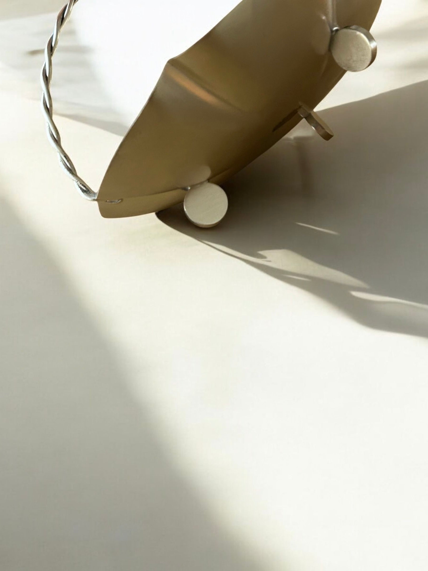 A vintage Art Deco Basket Bowl with a twisted handle and circular feet from Flock Studio in brass color sits on a light surface, casting a soft shadow. The lighting accentuates its smooth texture and sophisticated design, making it perfect for an elegant table setting.