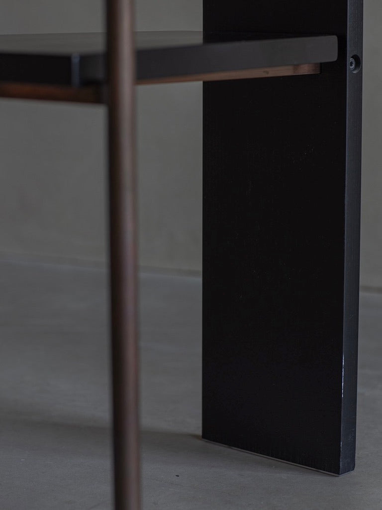 Close-up of a leg from the Jonas Bohlin - CONCRETE - black, by Bicci de' Medici, on a smooth concrete floor. The dark-toned leg's vertical and horizontal elements offer a modern, sleek look, with an elegantly blurred background focusing attention on the chair's design.