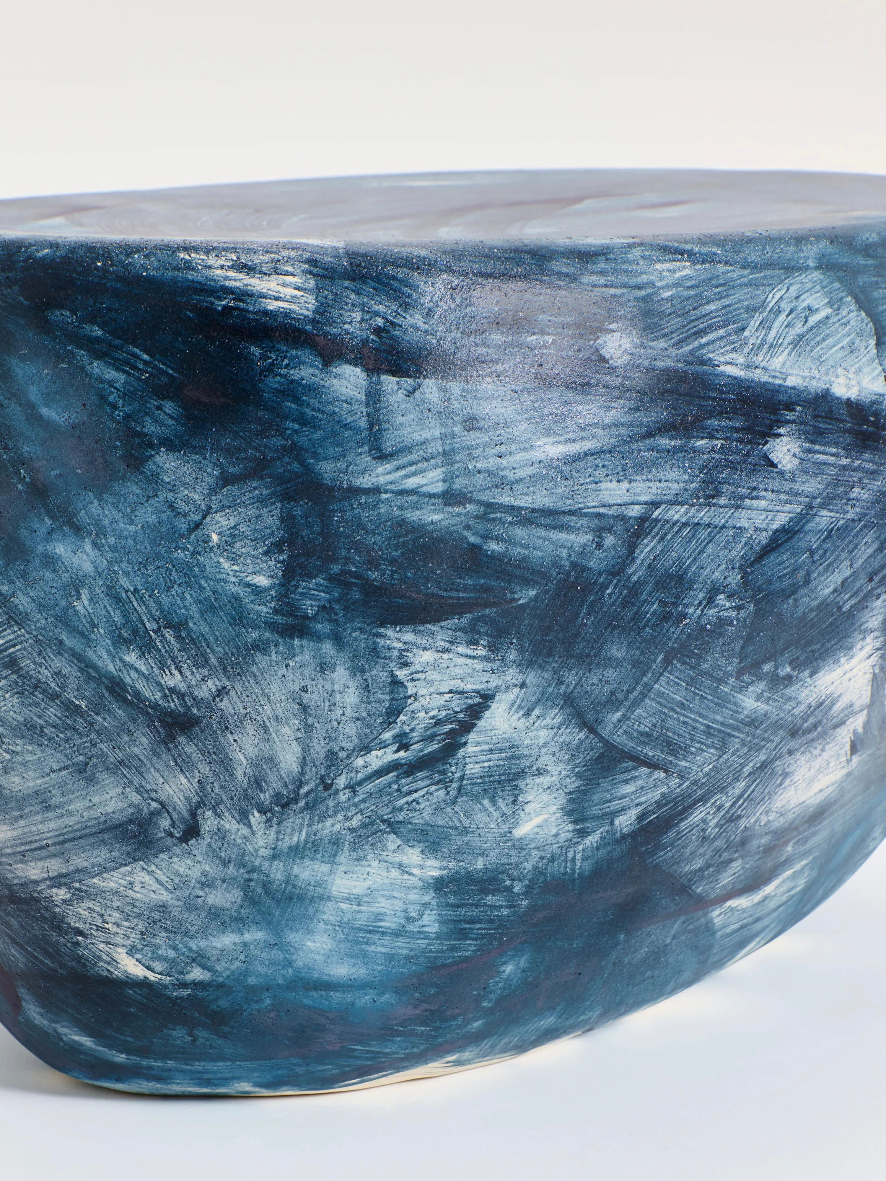 The Ceramic Coffee Table by Project 213A is a handmade piece with a smooth, rounded ceramic surface. It features swirling blue and white brushstrokes, adding texture and dynamism to the design. The custom glaze subtly reflects light beautifully off its surface.