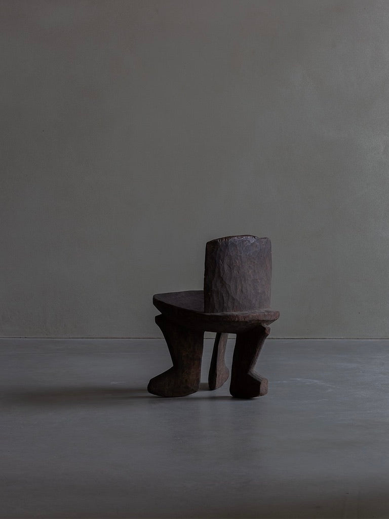 The African Stool by Bicci de' Medici, with its abstract primitive design and artistic irregular legs, stands boldly against a muted gray wall and light gray floor, adding elegance to the minimalist setting.