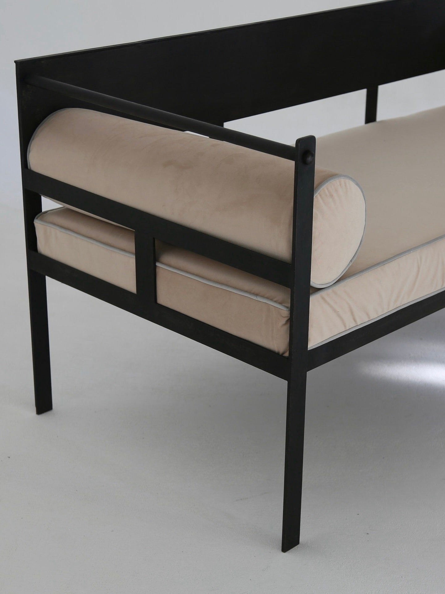 The Modernist Lounge Set by Ancien et Jolie is a minimalist sofa with a black metal frame, beige cushions, a cylindrical bolster, and a rectangular seat, echoing Mathieu Mategot's clean-line design style.