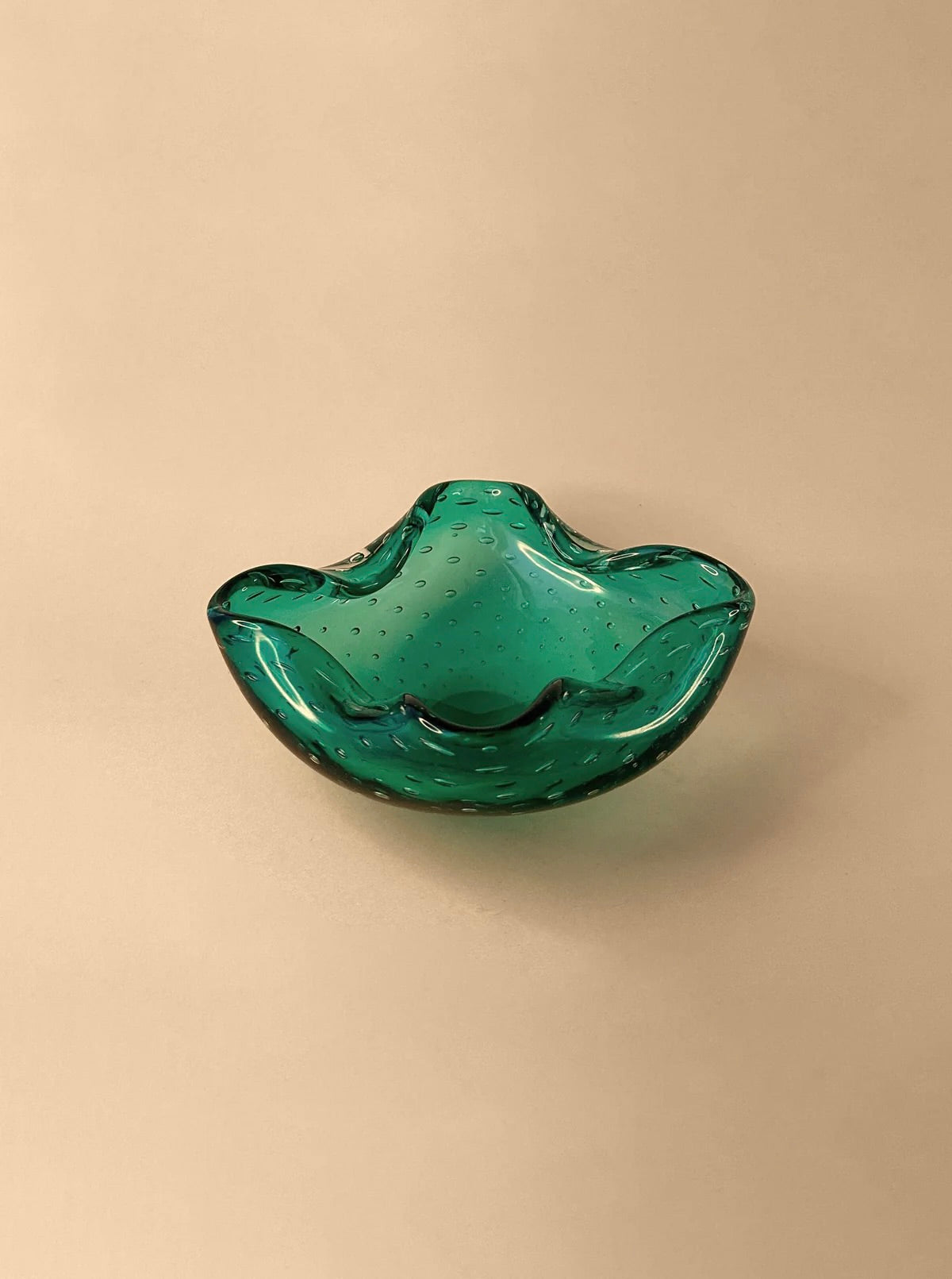 A decorative Mint Green 1960s Murano ashtray with bullicante bubbles from Dodo Vintage, reminiscent of the Barovier Toso style, sits on a smooth beige surface.