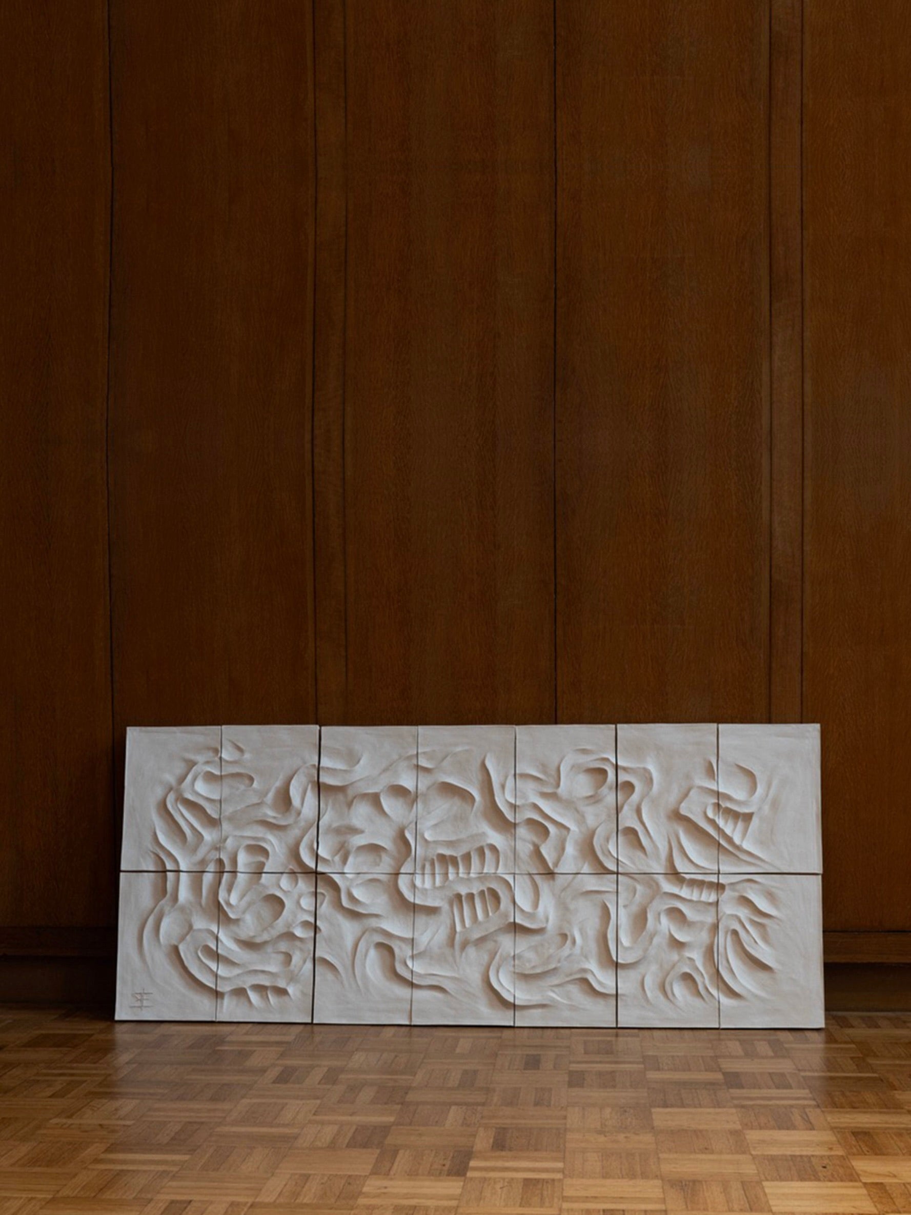 Le Grand Blanc - Wall Sculpture by Franck Scala from the RELIEFS collection displays abstract wavy patterns on white panels and leans against a large brown wooden wall, resting on parquet flooring for a warm, minimalist ambiance.