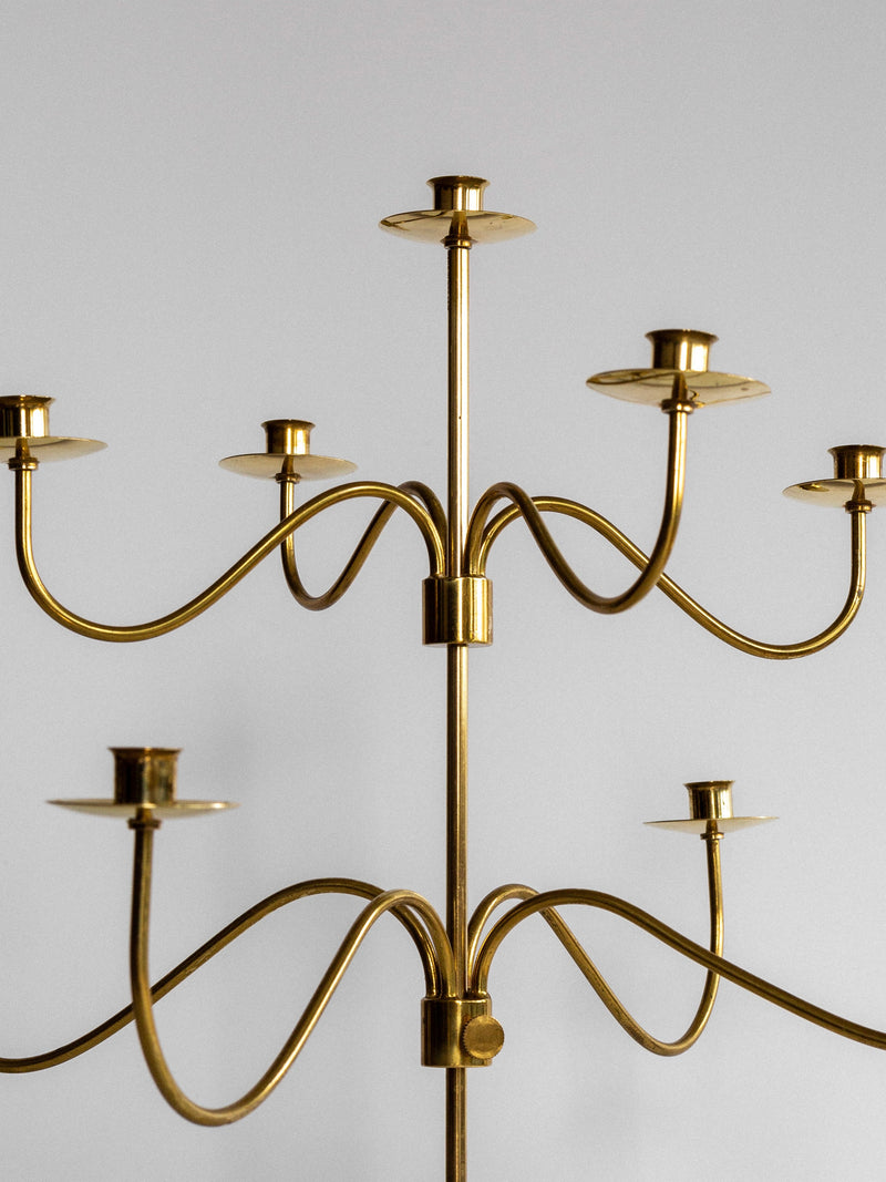 A Spigel "Large Mid-Century Brass Candelabra" with multiple arms and eight candle holders arranged in a circular fashion, set against a plain white background. Its sleek, minimalist design features smooth curves and clean lines reminiscent of a 1950s brass candelabra from Svenskt Tenn.