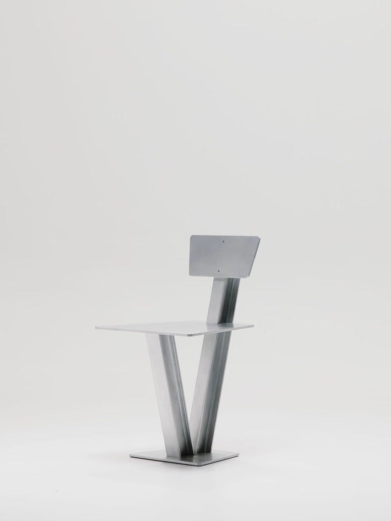 Introducing the Beam Chair by Marquel Williams: a modern minimalist masterpiece crafted from waxed aluminum, featuring a sleek geometric frame with flat seat and backrest supported by a V-shaped base on a square platform. Perfectly set against a plain white background.