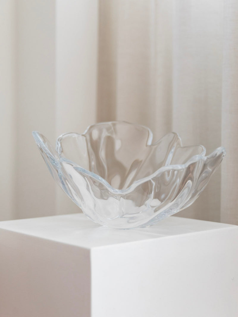 An XL Danish Vintage Crystal Glass Bowl by Lütken from Bottega Jacobs graces a white pedestal against a light beige curtain backdrop. Its form, echoing Per Lütken’s iconic vintage designs, features petal-like shapes with gentle curves and edges—a beautiful example of Danish crystal craftsmanship.