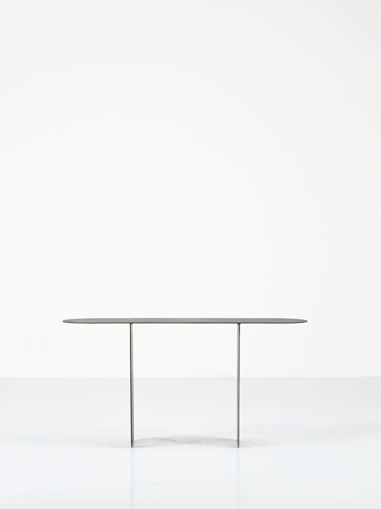 The Altar by COSEINCORSO features a minimalist black table with an oval top and two thin legs, set against a white background. Its sleek design creates a floating effect, reminiscent of limited edition small altars.