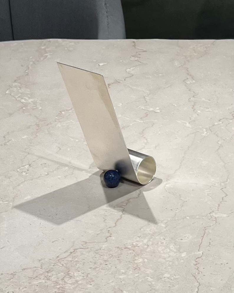 Silver plated brass phone holder with curved stand on marble surface