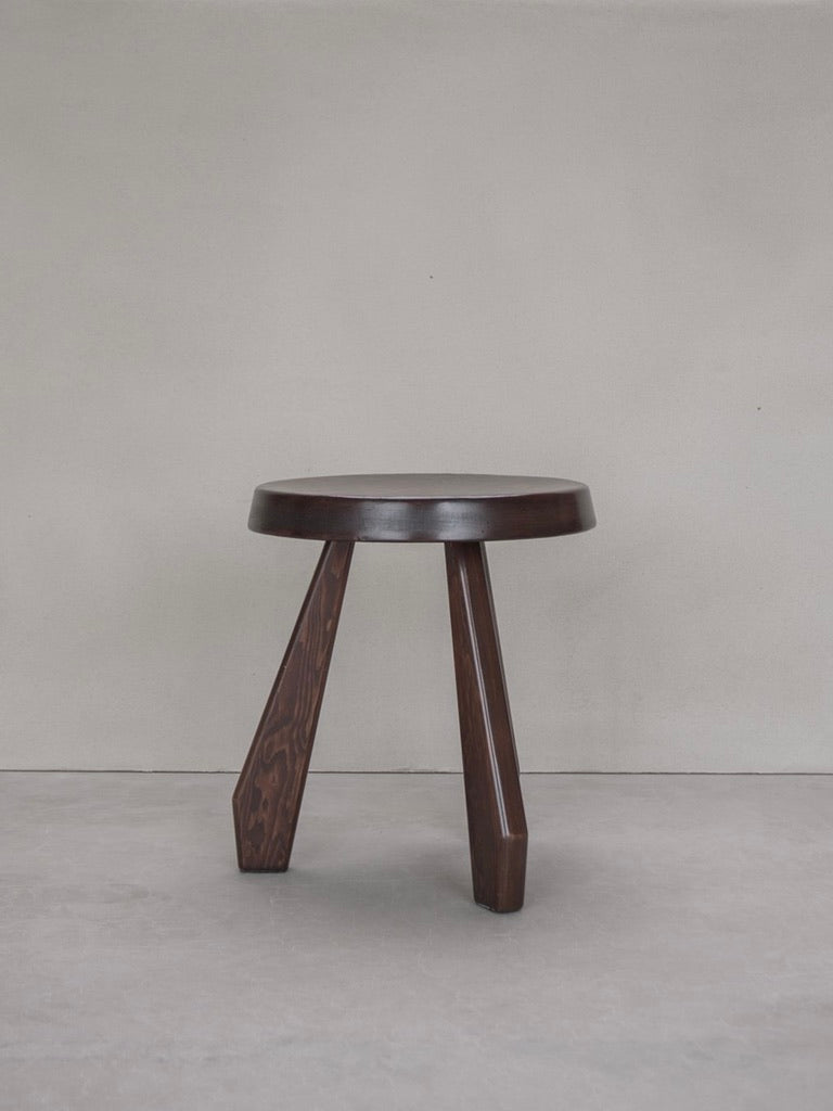 A modern Bicci de' Medici Charlotte Perriand - Sandoz Stool with three legs against a neutral gray background, featuring a round seat with a smooth finish, reflects timeless elegance in its minimalist design.