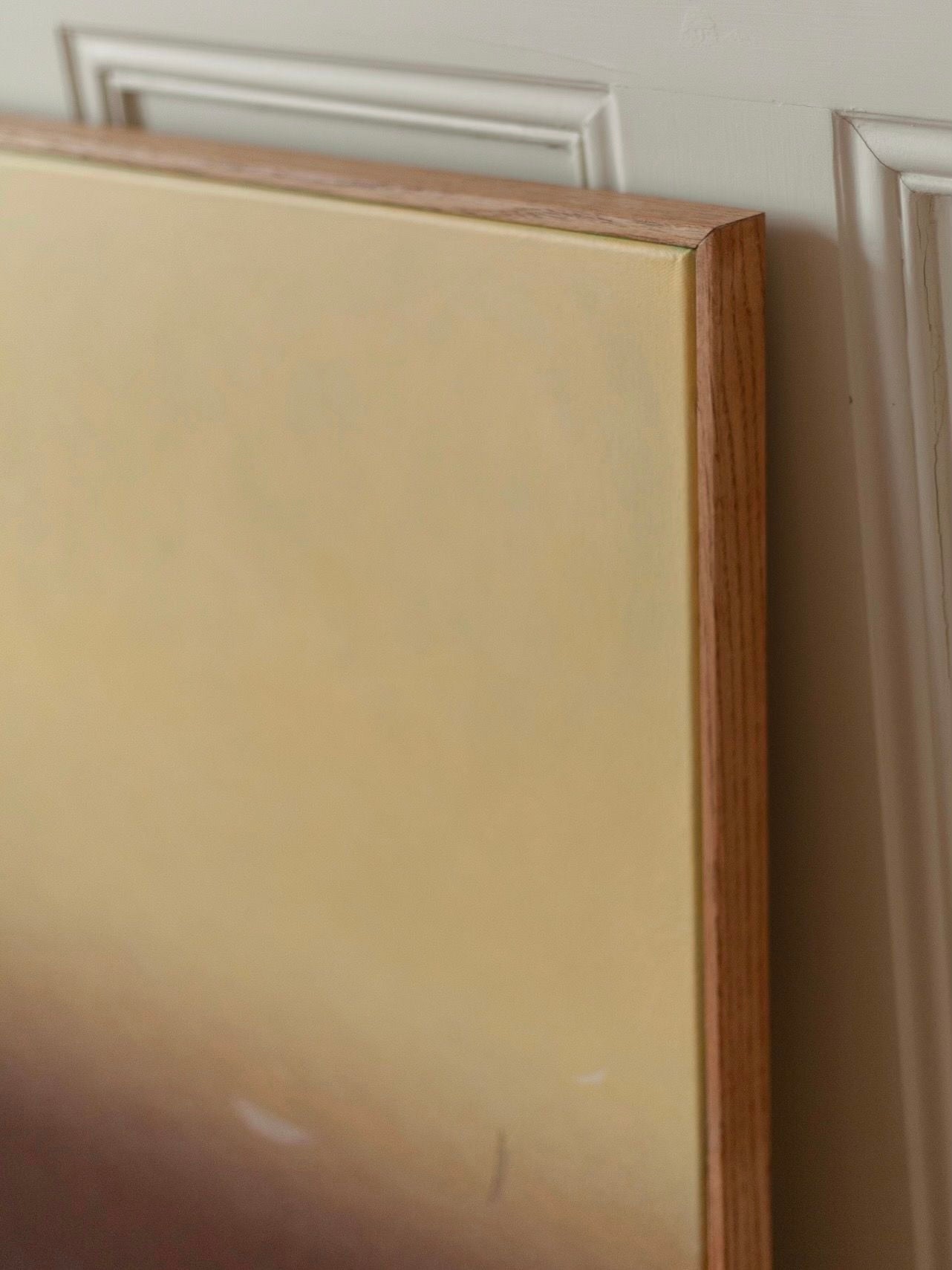 A close-up of the "Something(s) in the air", a 2024 acrylic on canvas painting by Rebecca von Matérn, is elegantly framed in light oak and resting against a wall. The artwork showcases a gradient with warm, earthy tones.