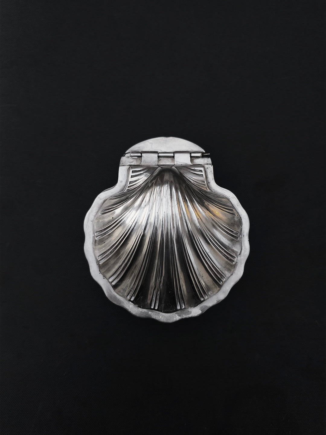 The Les Objoies Silver-plated Shell Box, shaped like a seashell with detailed ridges and a top hinge, beautifully rests against a black background, serving as an exquisite decorative container for any home decor.