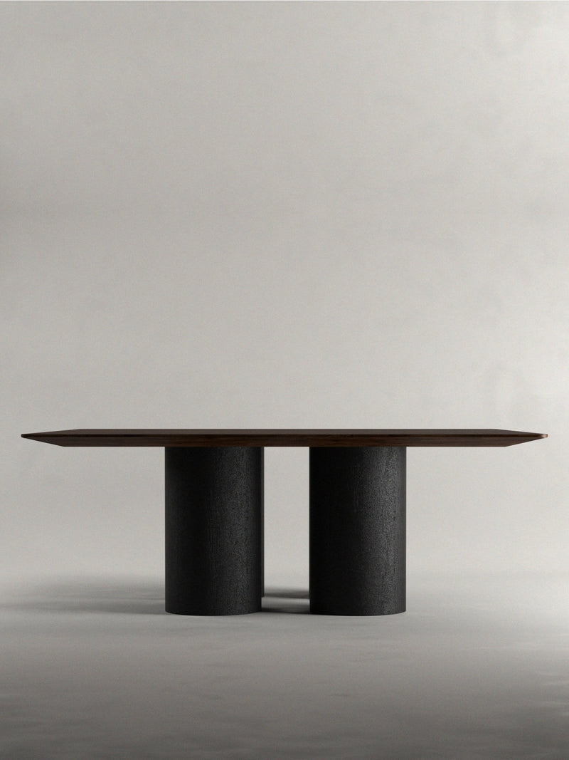 The 'Pier' Dining Table by Siete Studio has a dark walnut rectangular top and two large cylindrical black legs, set against a plain light gray background to enhance its modern, minimalist design.