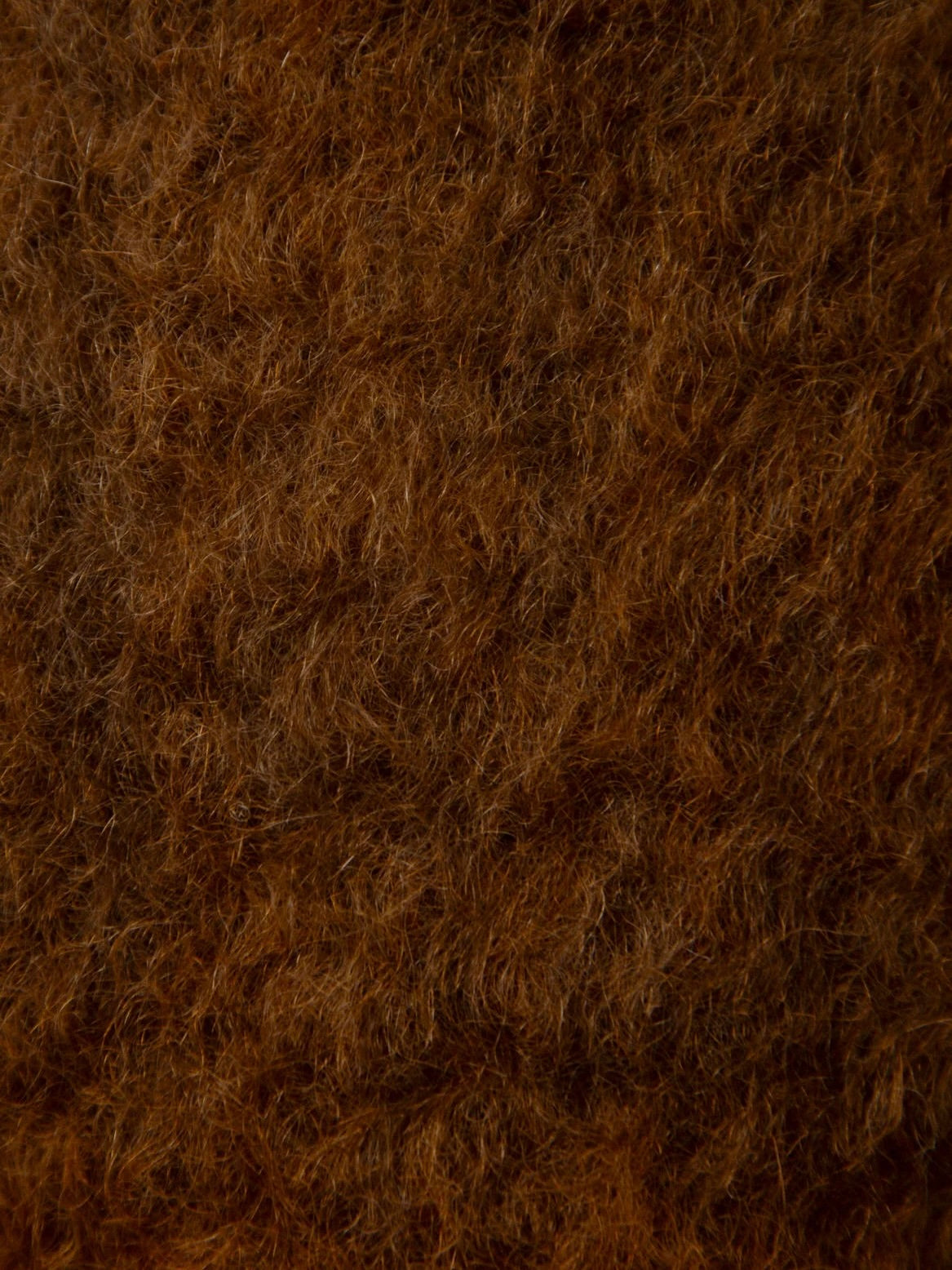 The "Arbor Sable" Throw by The Wren features a close-up texture of woolly fibers with a slightly curly and dense appearance, reminiscent of a luxurious mohair blanket. Its rich, deep brown color with subtle variations creates a soft and cozy, eco-friendly look.