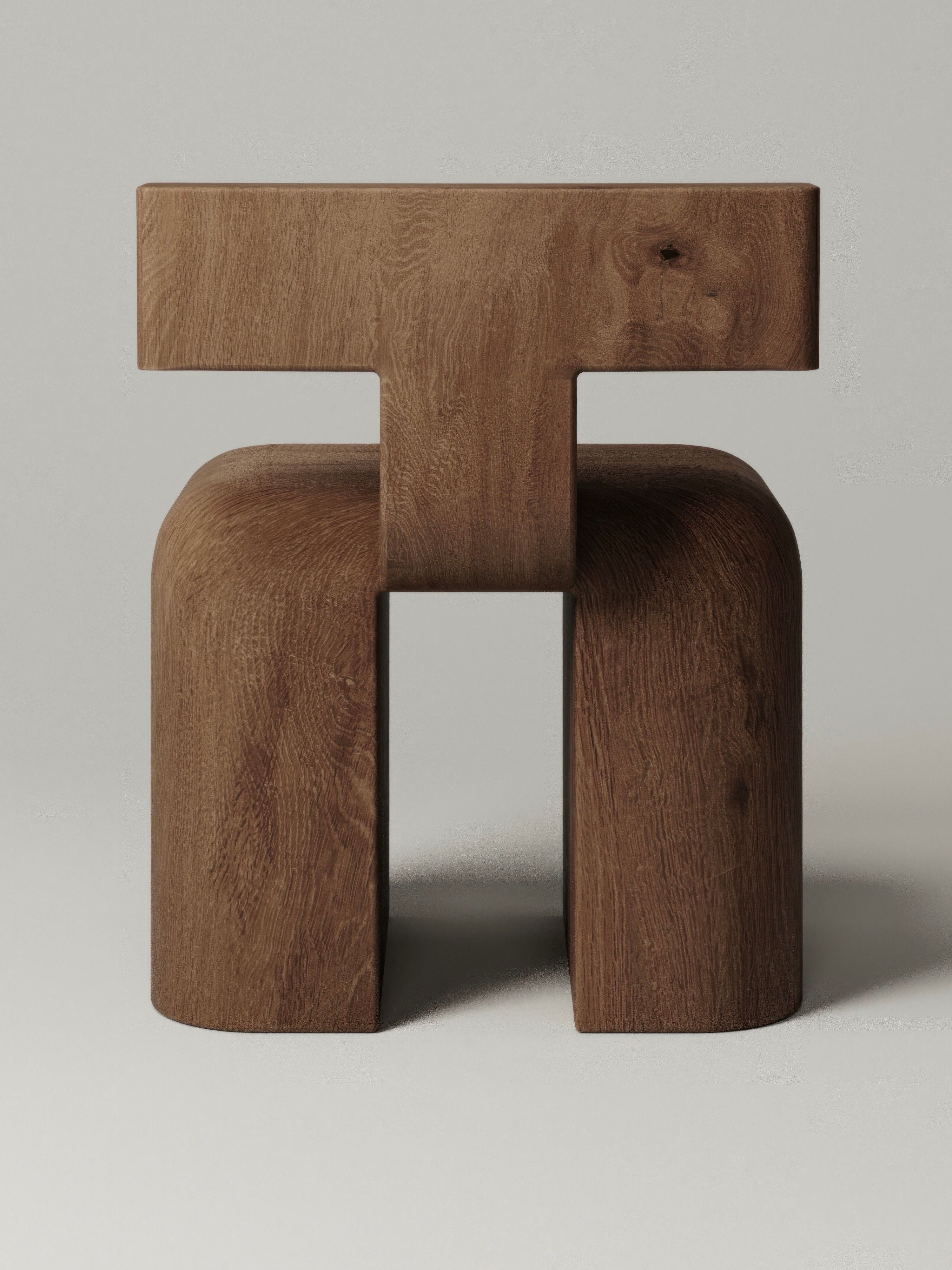 The Monolith M_013 Accent Chair is a striking wooden piece with a modern design, featuring a thick, horizontal top and sturdy legs that form an abstract "H" shape. The negative space showcases the wood's rich grain and finish beautifully against any plain background.