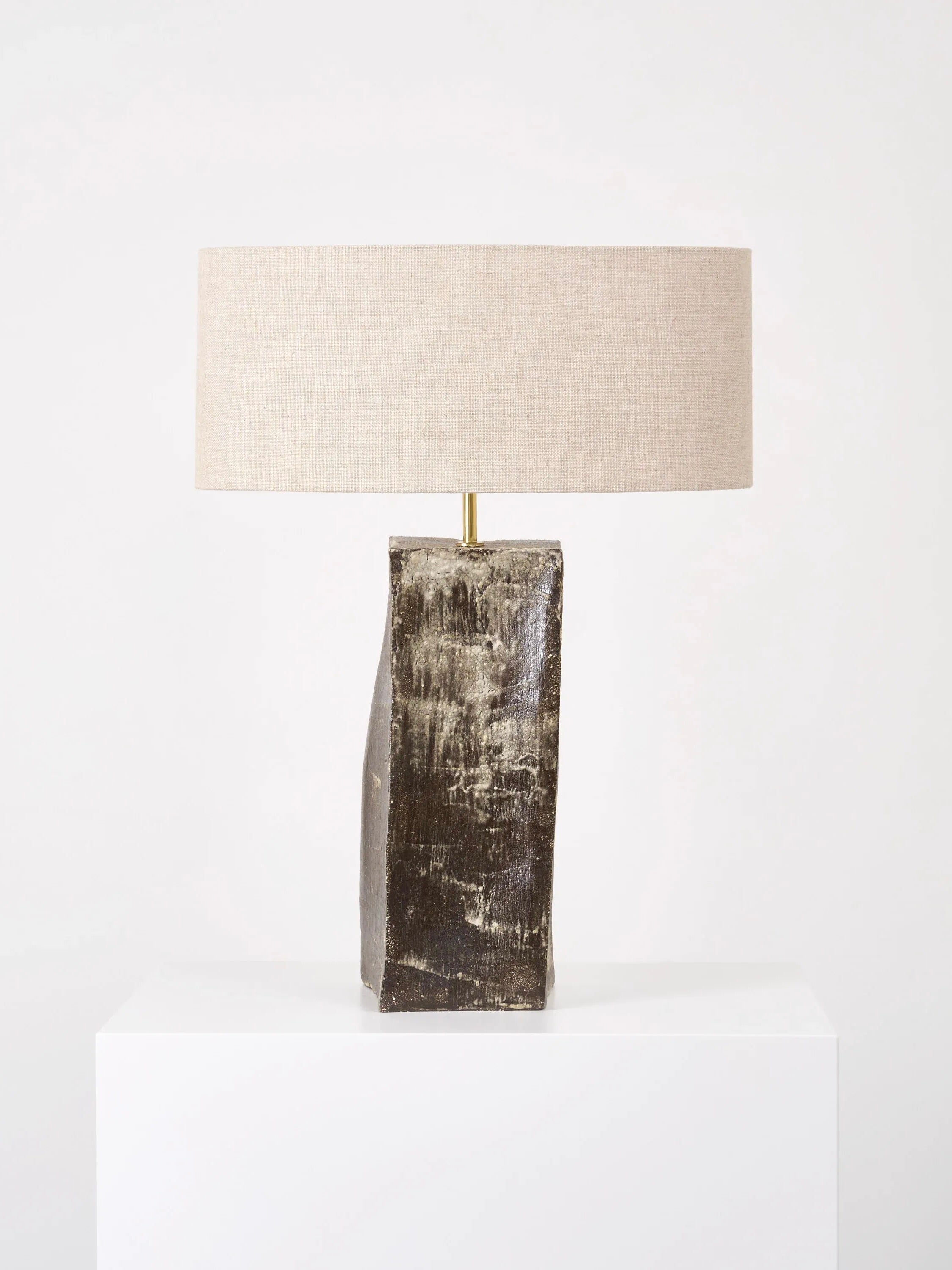 A modern handmade lamp from Project 213A, featuring a textured dark brown rectangular ceramic base and a large round beige fabric shade, sits on a white surface against a plain white background.